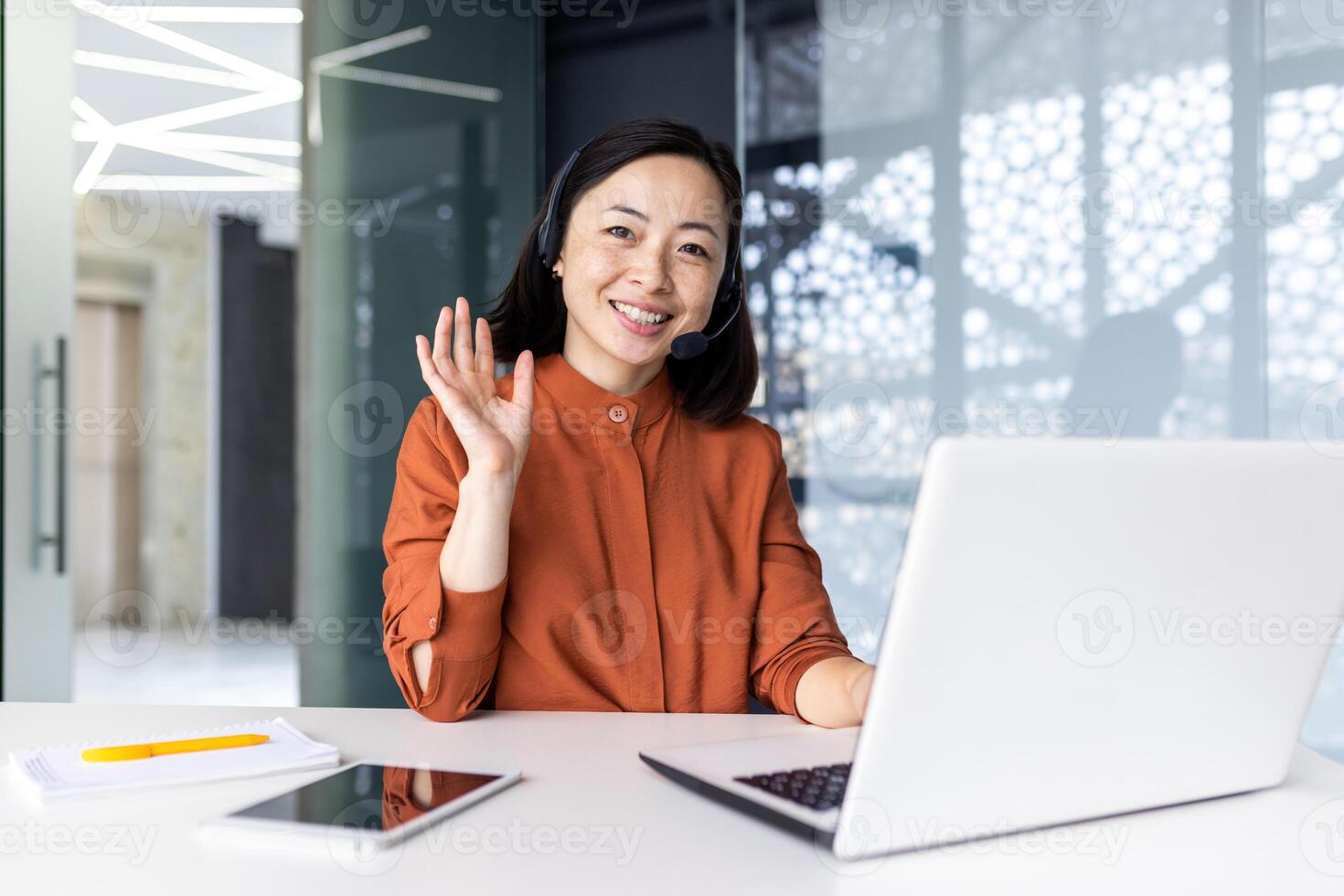 Portrait of successful tech support worker, Asian woman looking at camera, businesswoman with headset for call, greeting gesture, inside office with laptop. photo