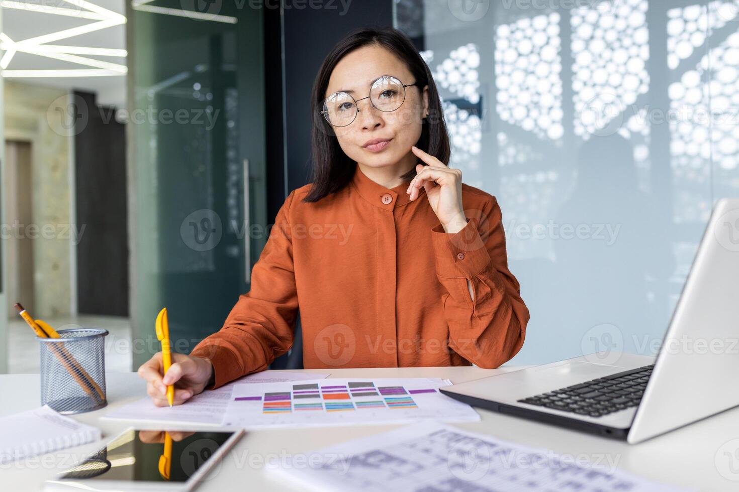 Portrait of confident serious asian business woman financier inside office at workplace, worker behind paperwork looking thoughtfully at camera, working with documents bills and graphs. photo