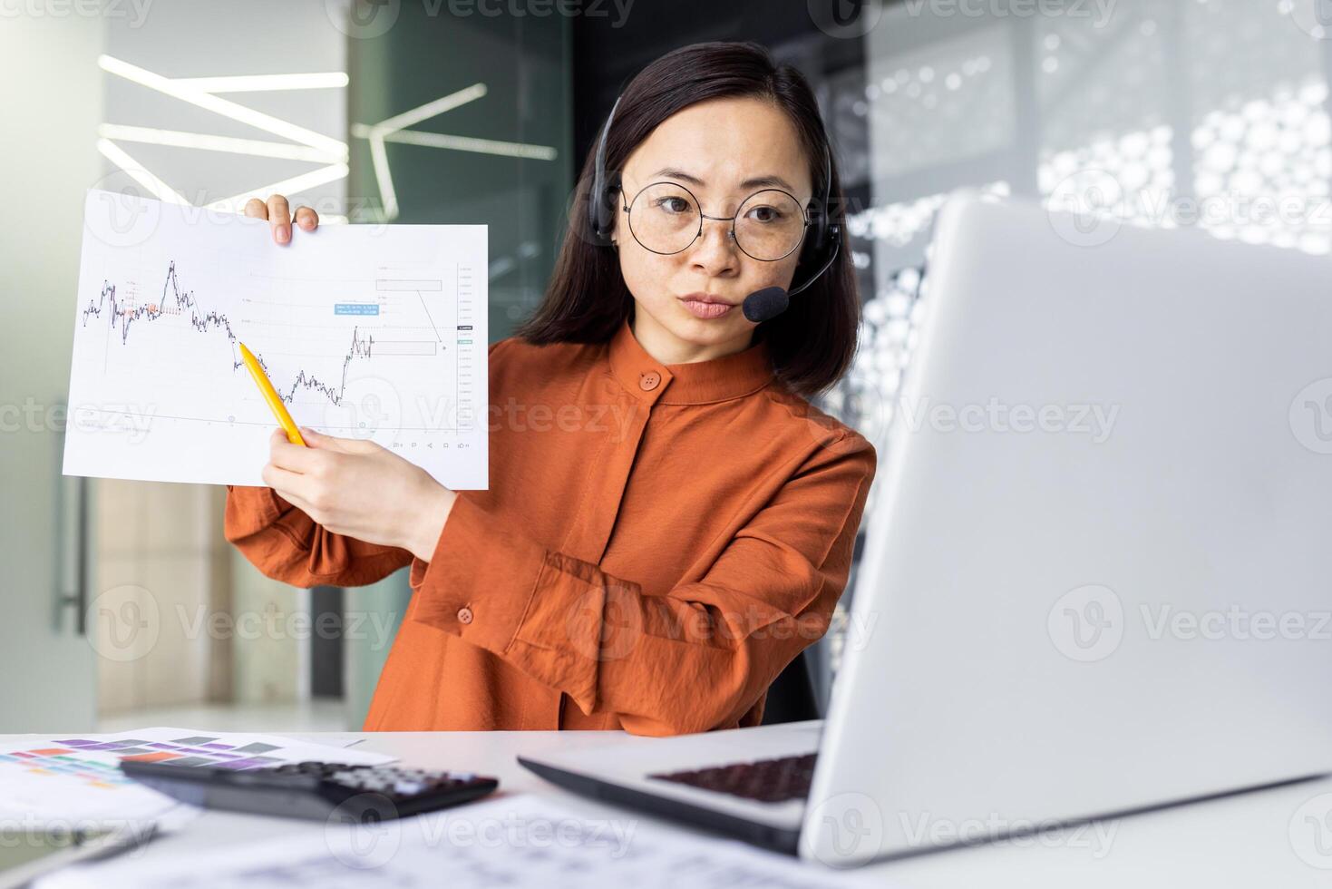 Serious concentrated thinking woman on online presentation, meeting, business woman focused showing to camera laptop income graph of new project, working with headset phone inside office. photo