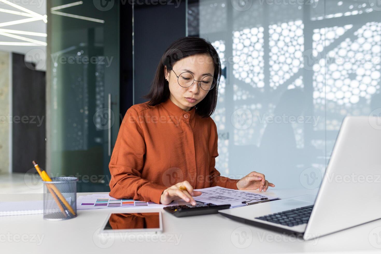 Confident serious concentrated and focused business woman behind paper work inside office, woman with calculator thinking checking accounts financial reports, Asian with laptop preparing documents. photo