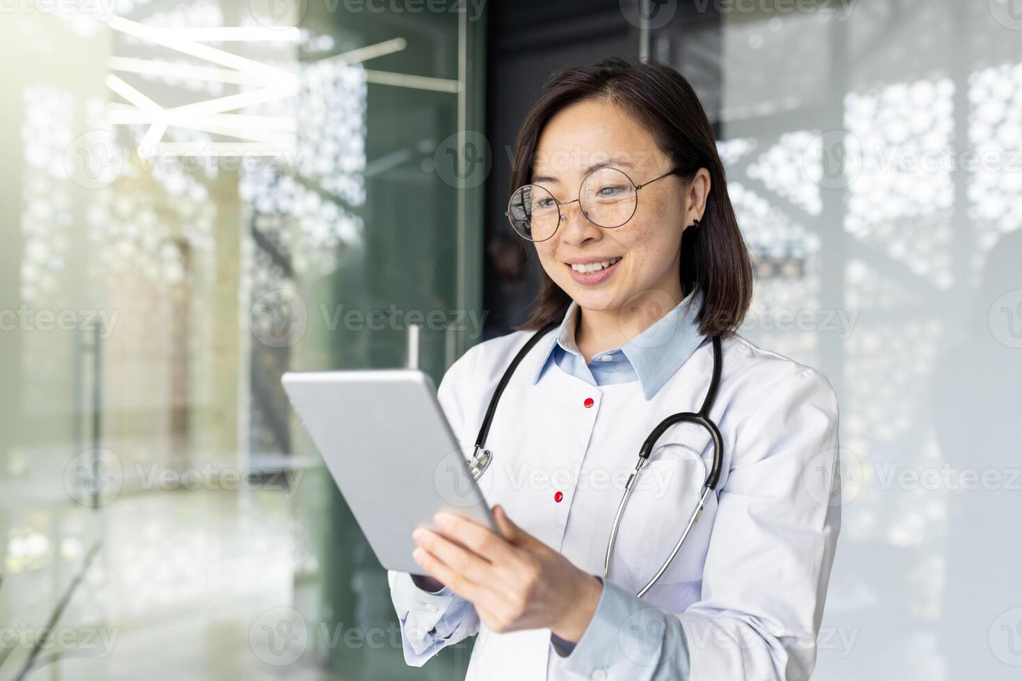 Smiling Asian female doctor in clinic office provides remote consultations using a tablet, symbolizing modern healthcare. photo