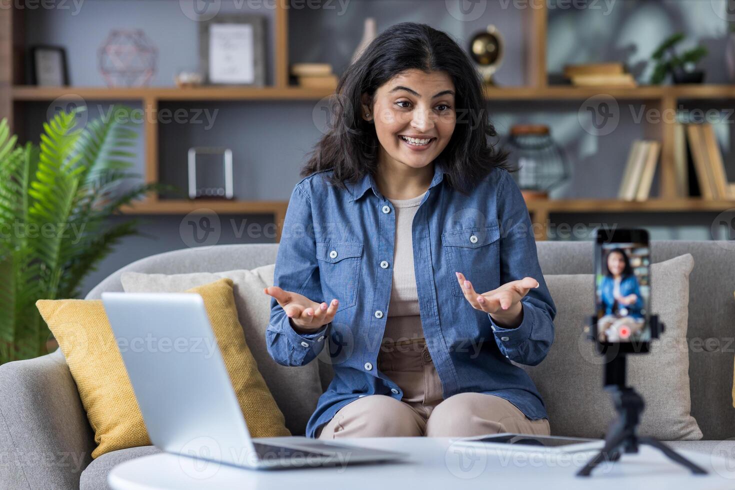 A woman enthusiastically gestures while speaking to the camera, recording a blog at home. photo