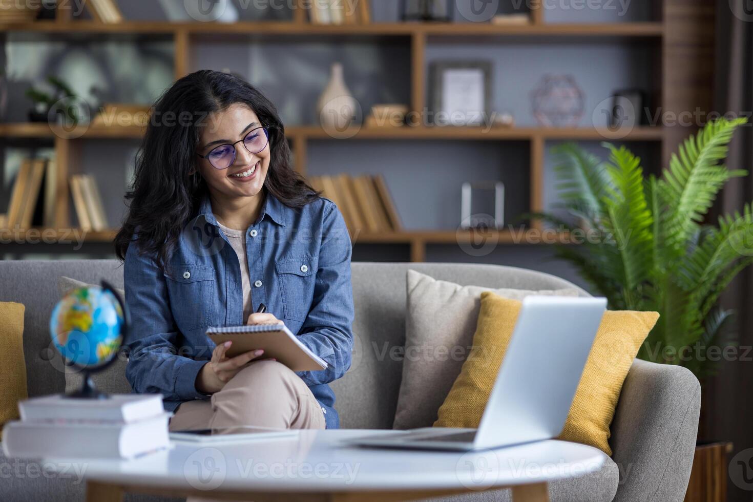 Distance learning and studying. Young smiling Indian woman sitting on sofa at home, talking on call and taking notes in notebook. photo
