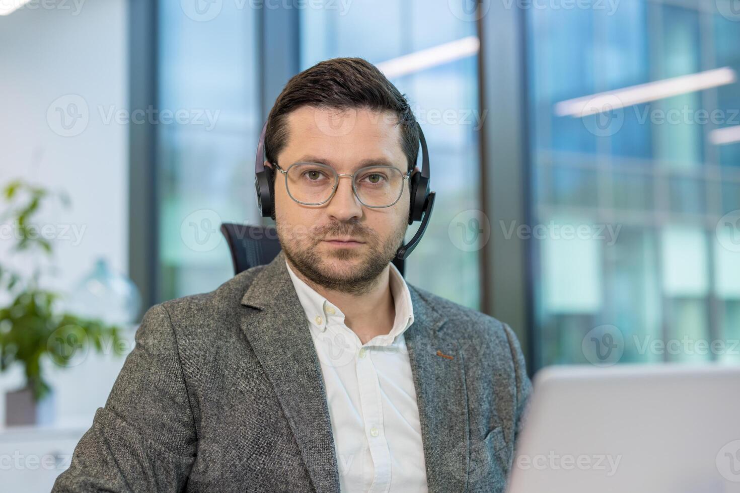 A man in a gray suit and headset looks directly at the camera, possibly working in a customer service or call center. photo