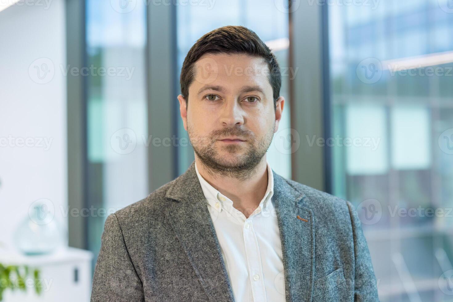 Close-up portrait of a serious young man in a suit standing in the office, looking confidently at the camera. photo