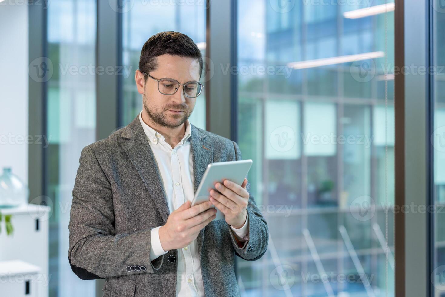 Office worker, young man in a suit standing indoors and using a tablet. photo