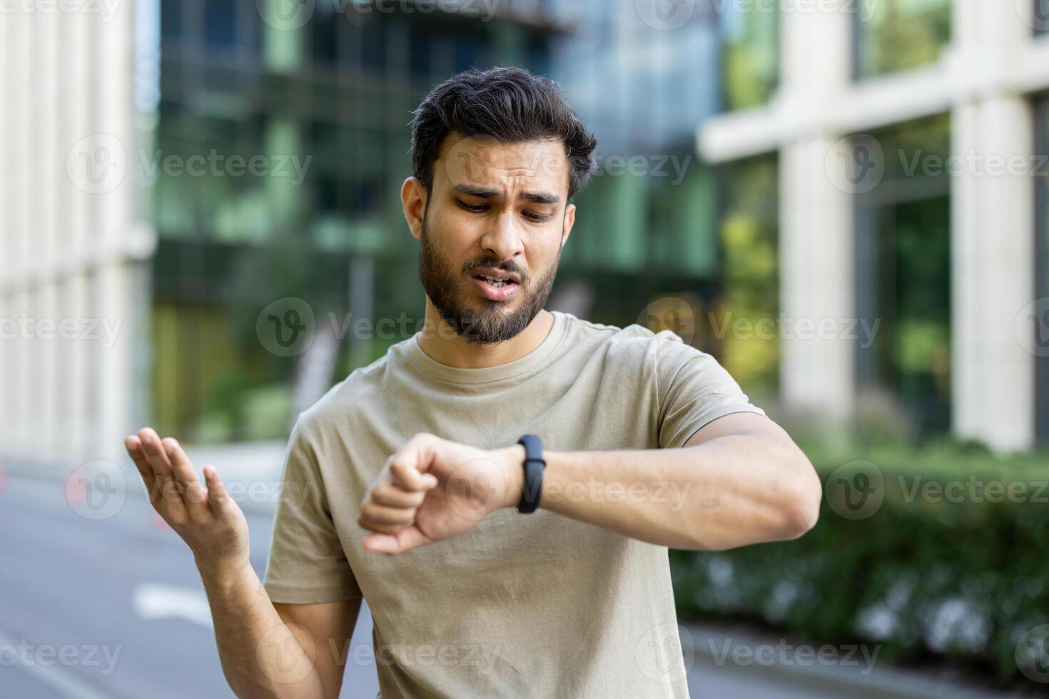 A young man looks at his watch while gesturing. Possibly running late, or tracking fitness activity during exercise. photo