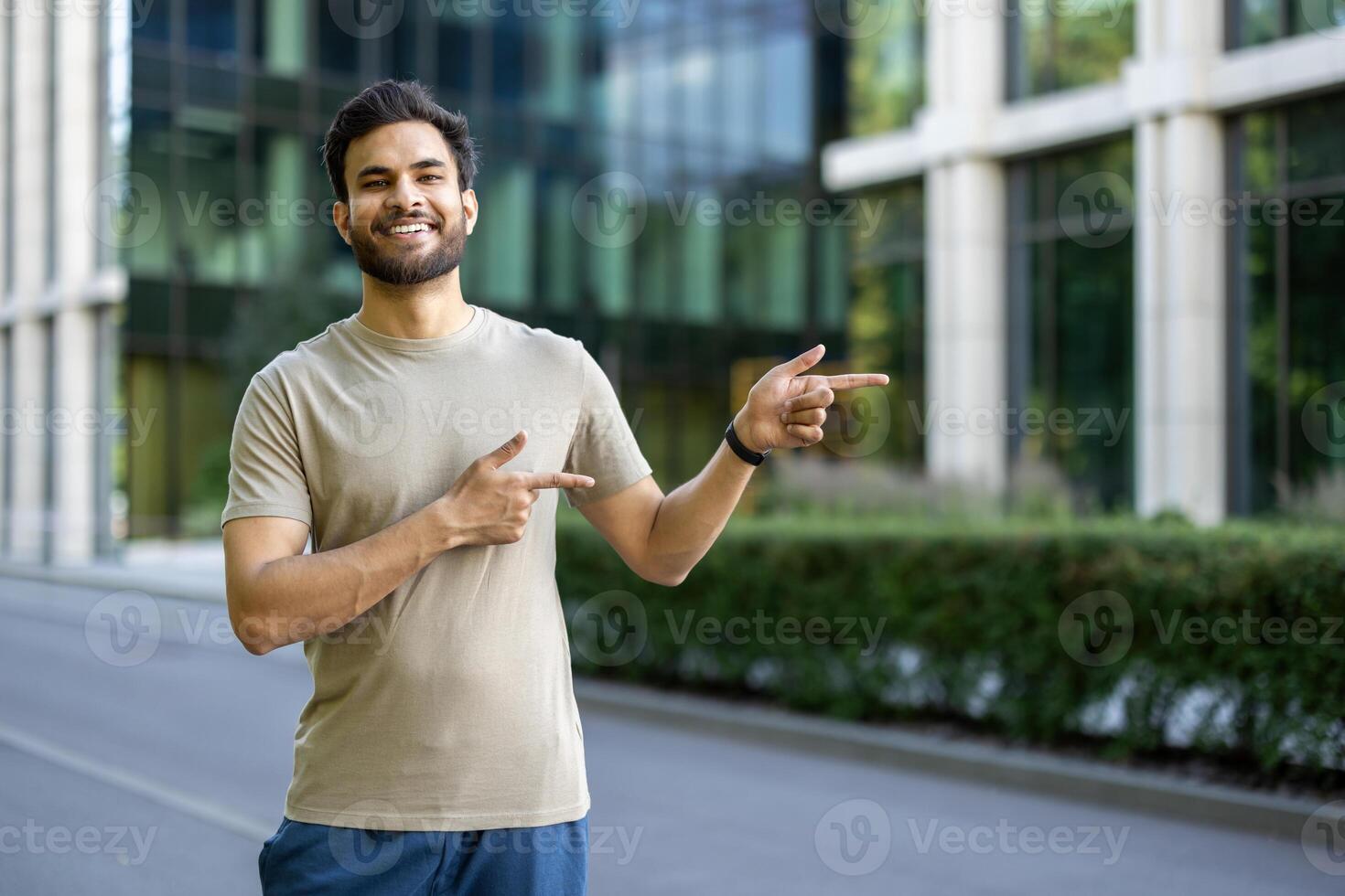 A young man in casual wear points towards something, smiling confidently with a building in the background. photo