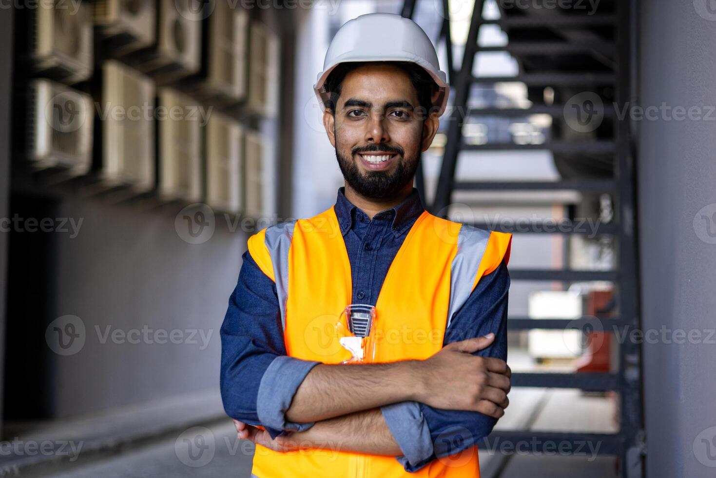 Portrait of young successful engineer worker, man smiling and looking at camera, wearing hard hat and vest, working in factory plant. photo