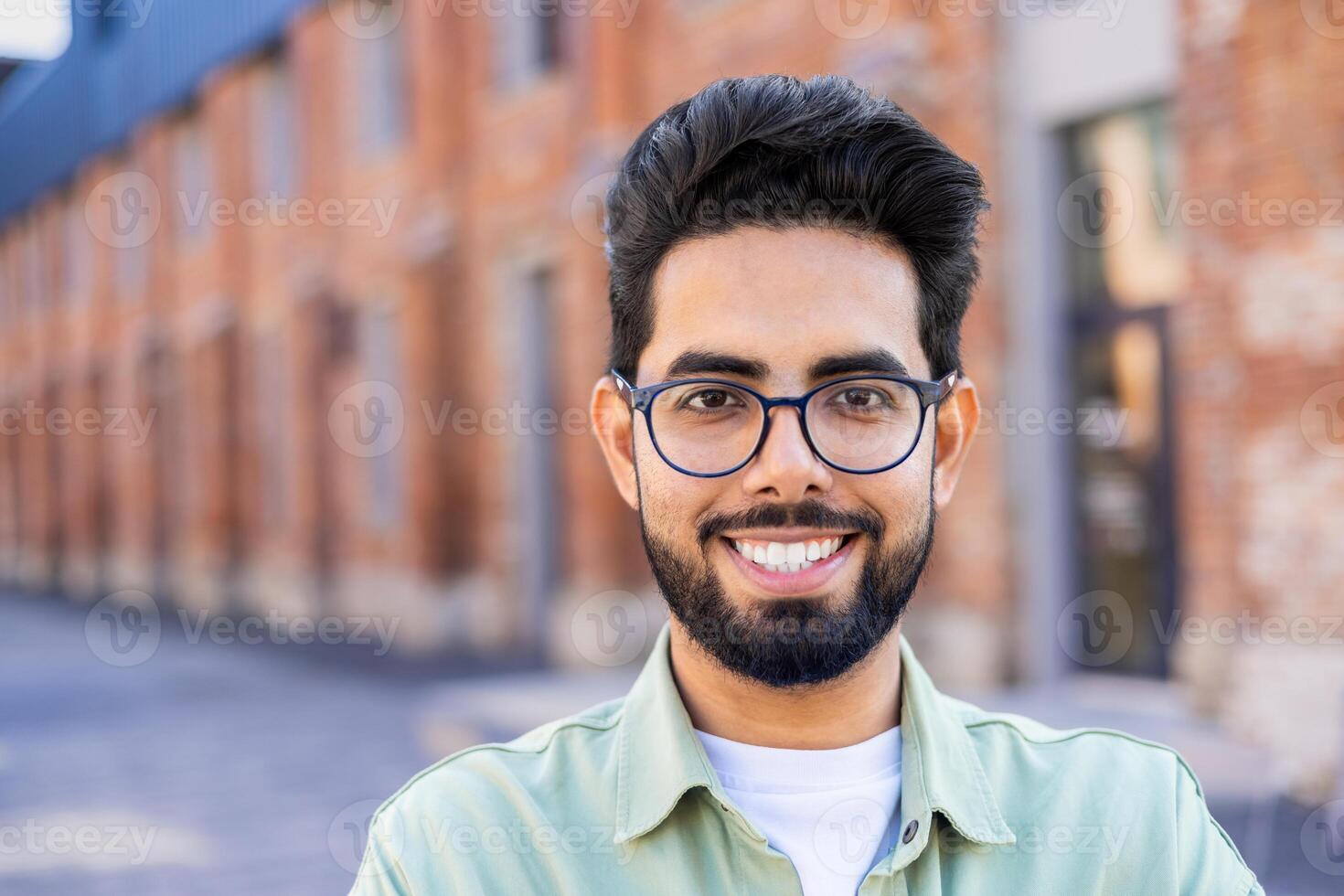 Close-up portrait of a young Hindu man standing on the street near a building, smiling widely and looking at the camera photo