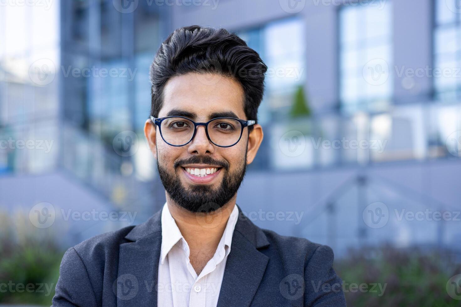 A young Indian businessman in a sharp suit stands confidently outdoors with an urban landscape in the background. Ideal for corporate diversity themes. photo
