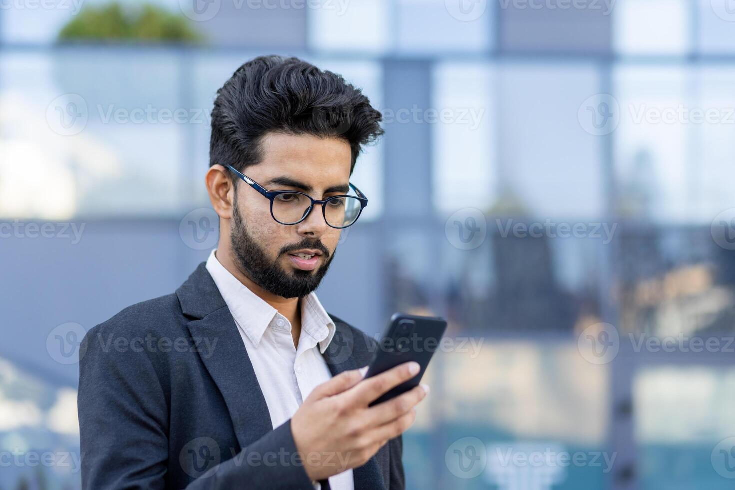 A young professional stands outdoors in a suit, focused on his smartphone. This image captivates modern business communication in an urban environment. Perfect for depicting connectivity and entrepreneurship. photo