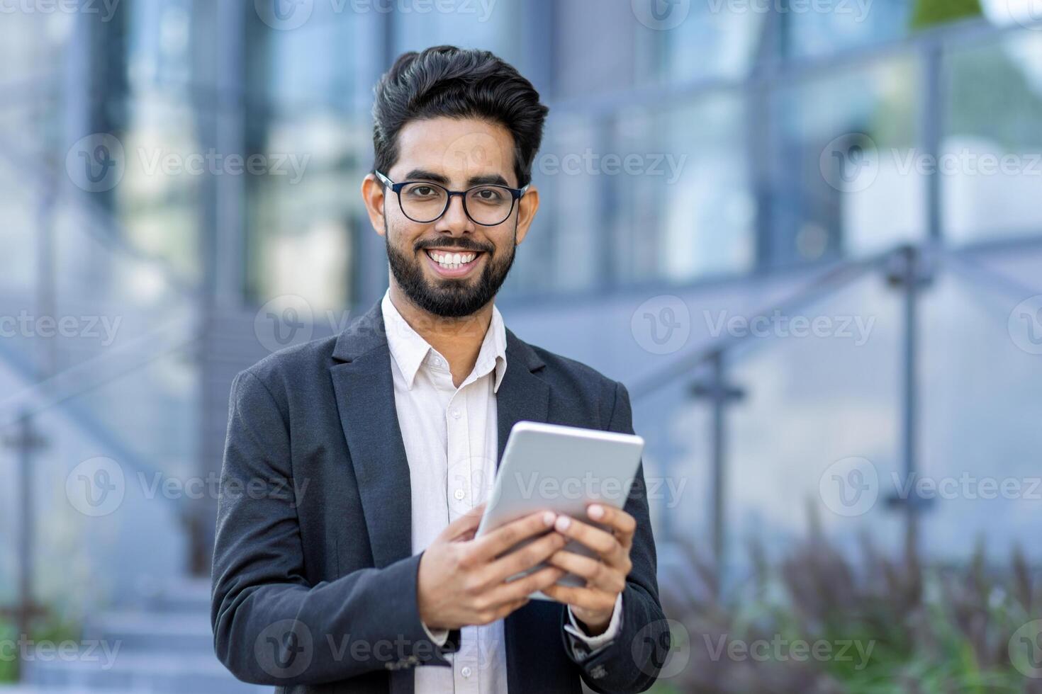 A young businessman in a smart suit engrossed in using his tablet computer. Captured outside a contemporary office setting, symbolizing global business and connectivity. photo
