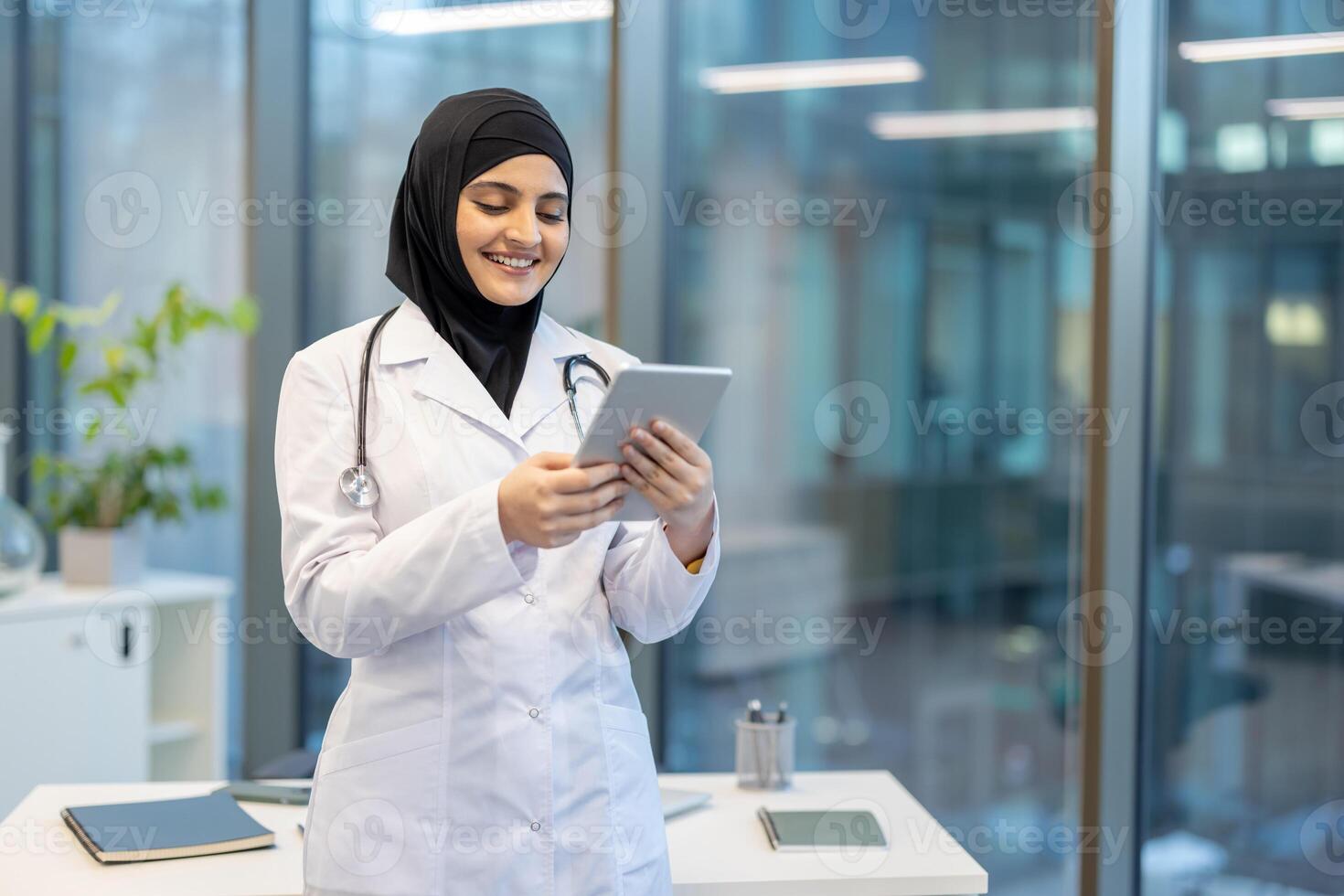 A smiling female doctor in a hijab reviews a tablet in a modern office setting. photo