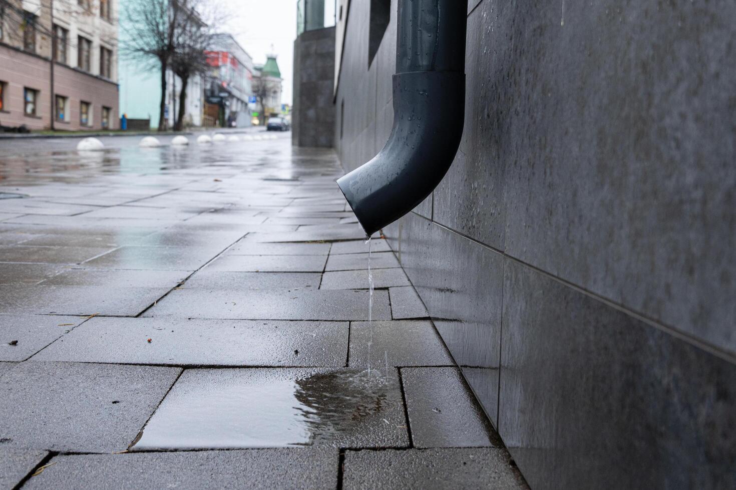 Water flows from a downspout onto the glossy, wet pavement in an urban setting during a rainy day, capturing the feel of a quiet street photo