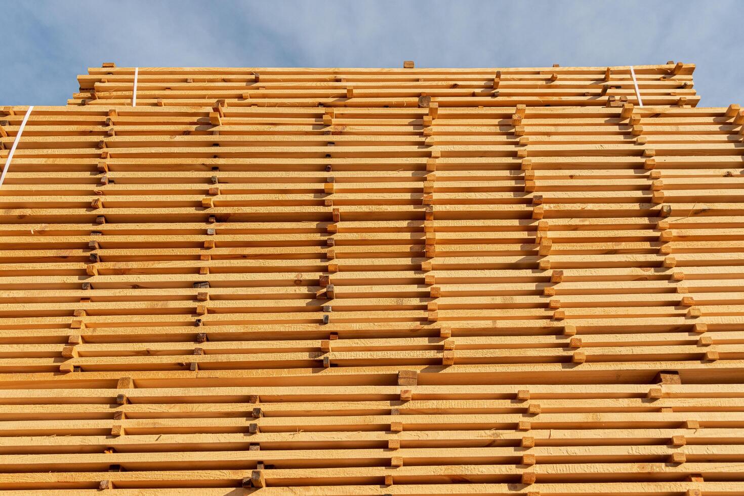 A collection of wooden planks is carefully stacked at a construction site, showcasing their texture and arrangement against a blue sky photo