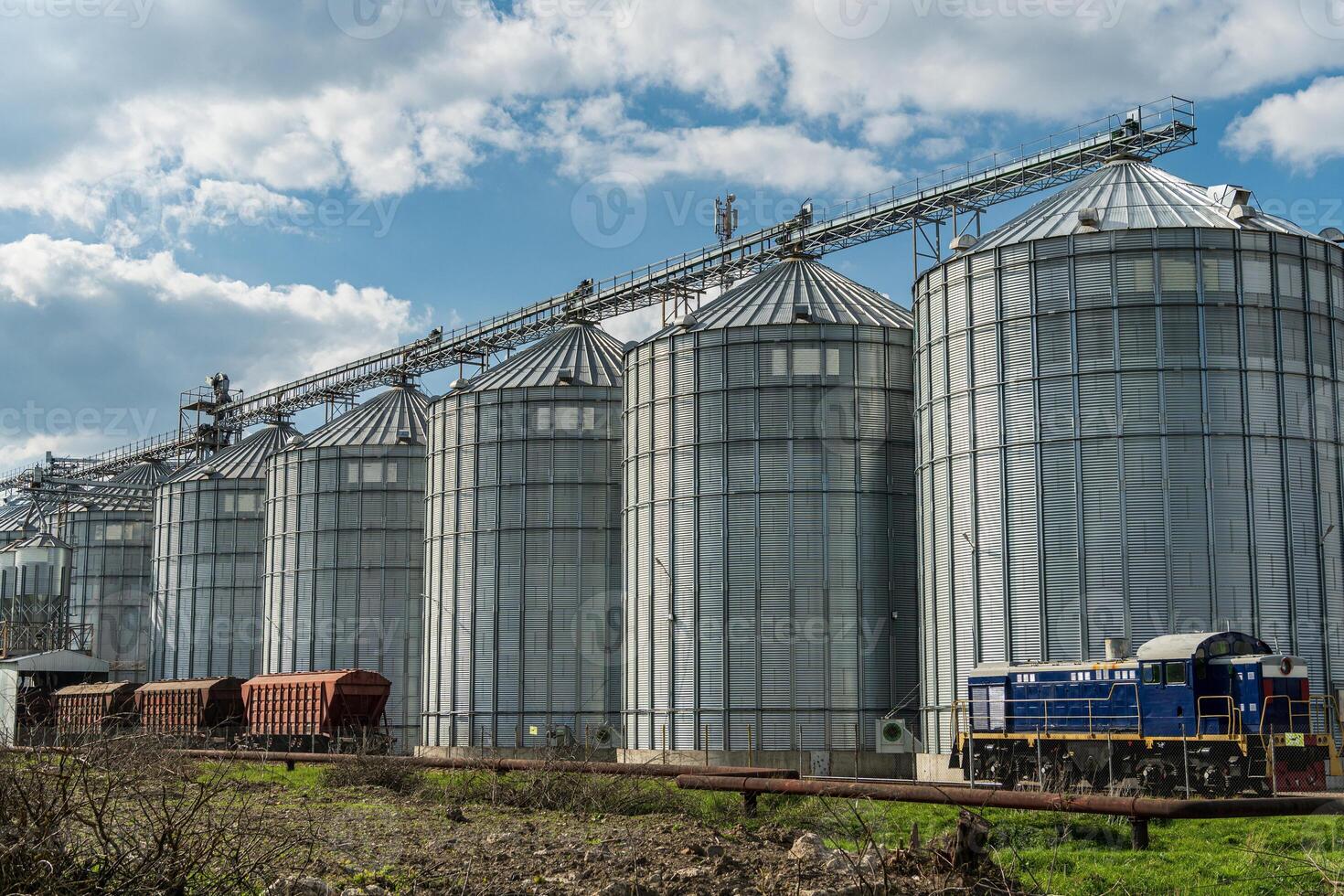 Tall silos stand at a grain storage facility, filled with harvested crops and situated alongside a railway, showcasing the farming industry photo