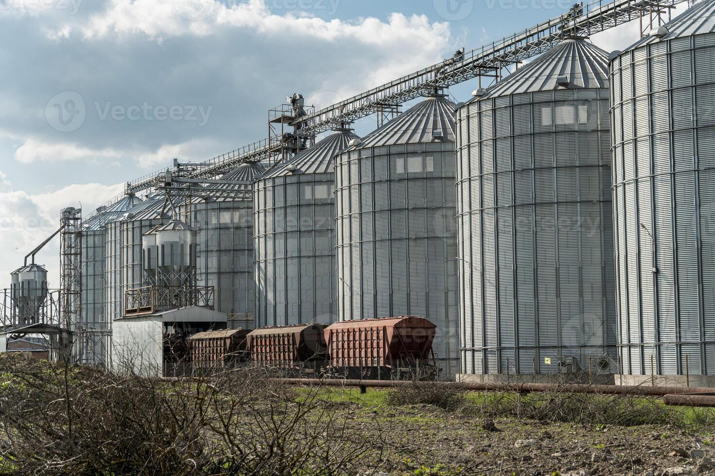 Large metal silos stand strong at an agricultural site, storing harvested grain while train cars wait nearby to transport the crop to market photo
