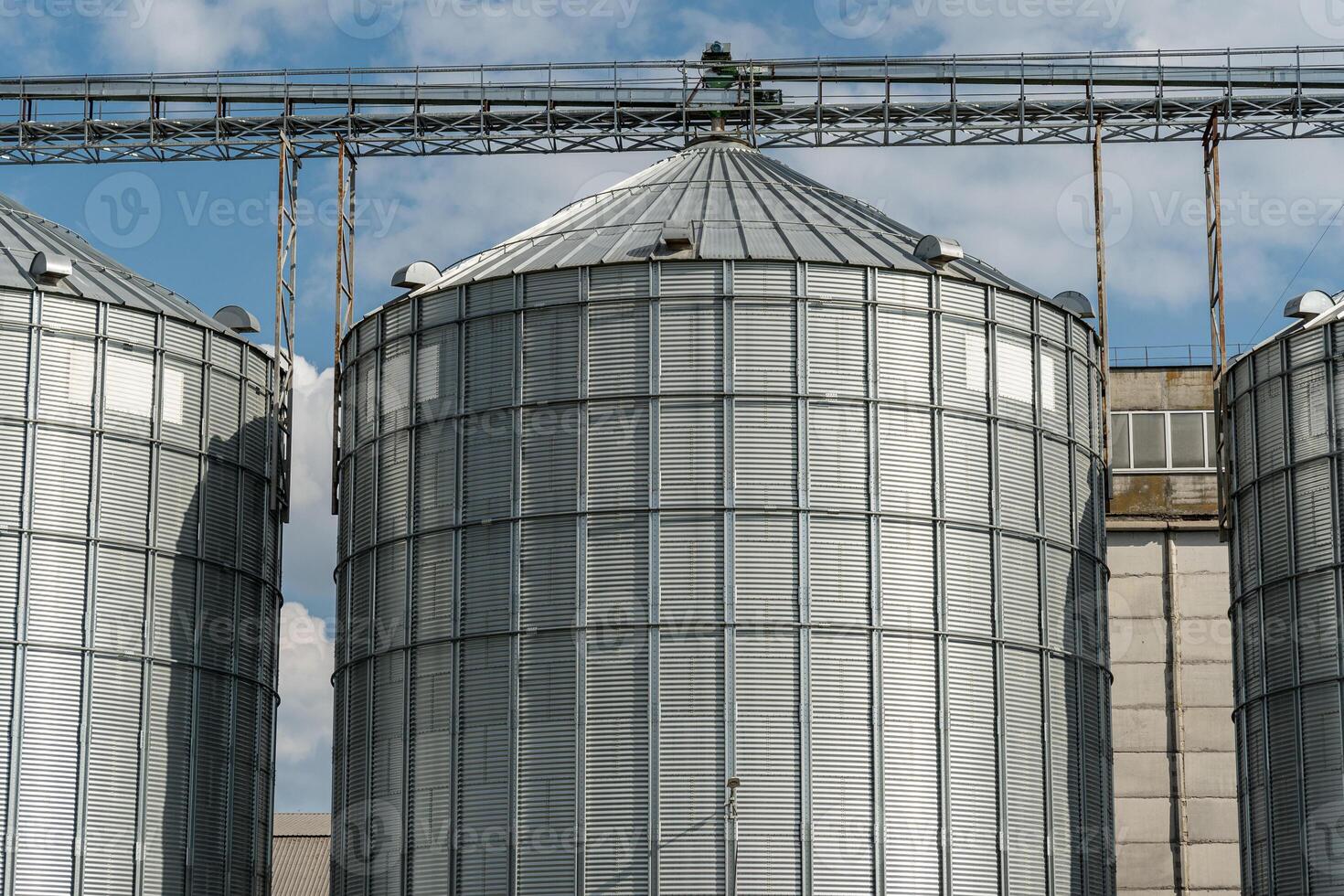 Metal silos stand tall at a crop storage facility, ready for grain harvest as clouds drift by on a sunny day in the countryside photo