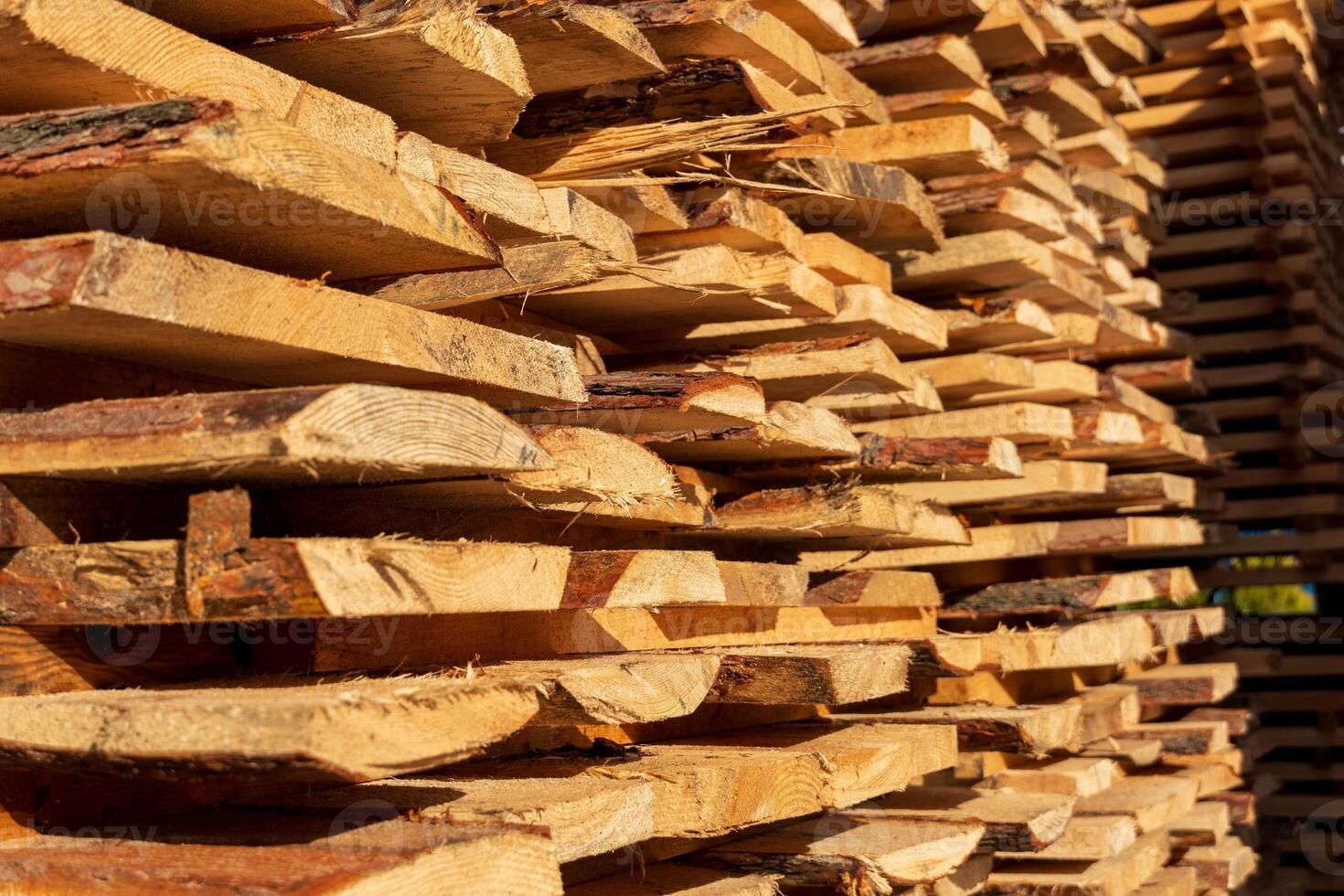Planks of timber are neatly stacked, showcasing rich textures and warm colors as sunlight filters through at a sawmill photo