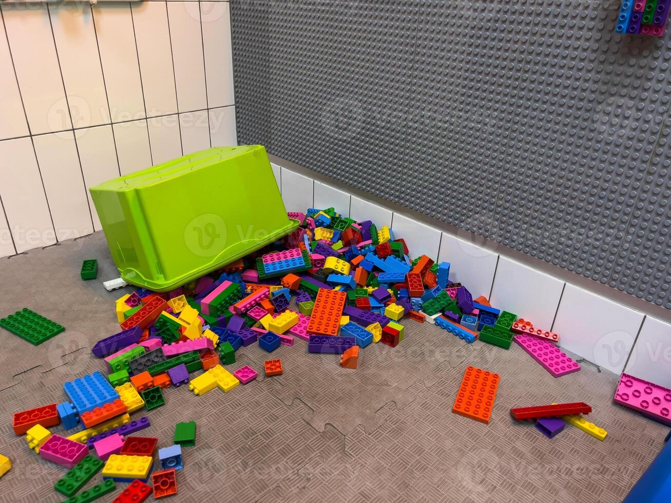 Brightly colored building blocks are spread across the floor near a green storage box, creating a playful mess in a children's play area photo
