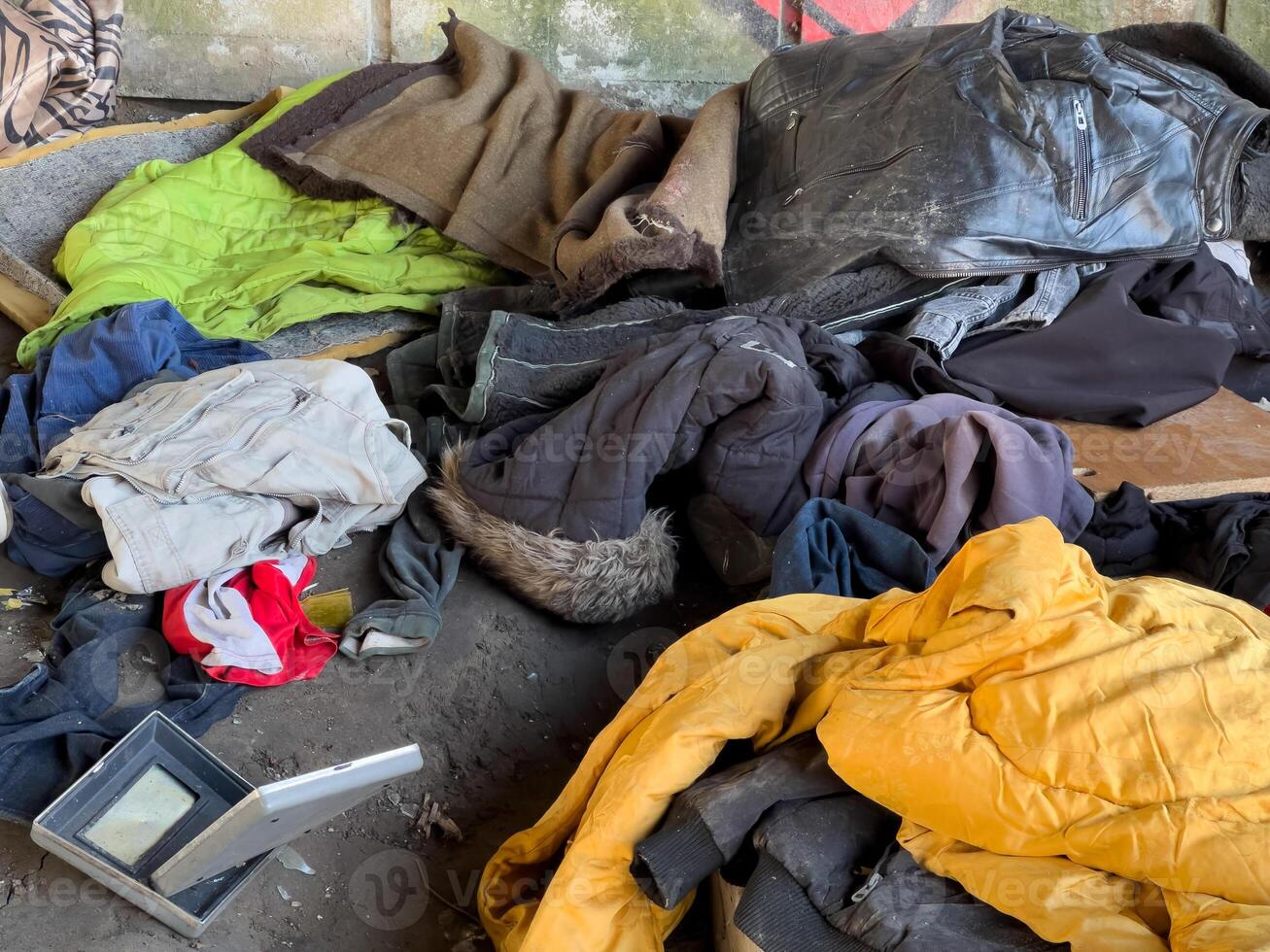 A pile of various clothing items lies on the ground in a dilapidated space, indicating neglect and lack of care in daylight hours photo