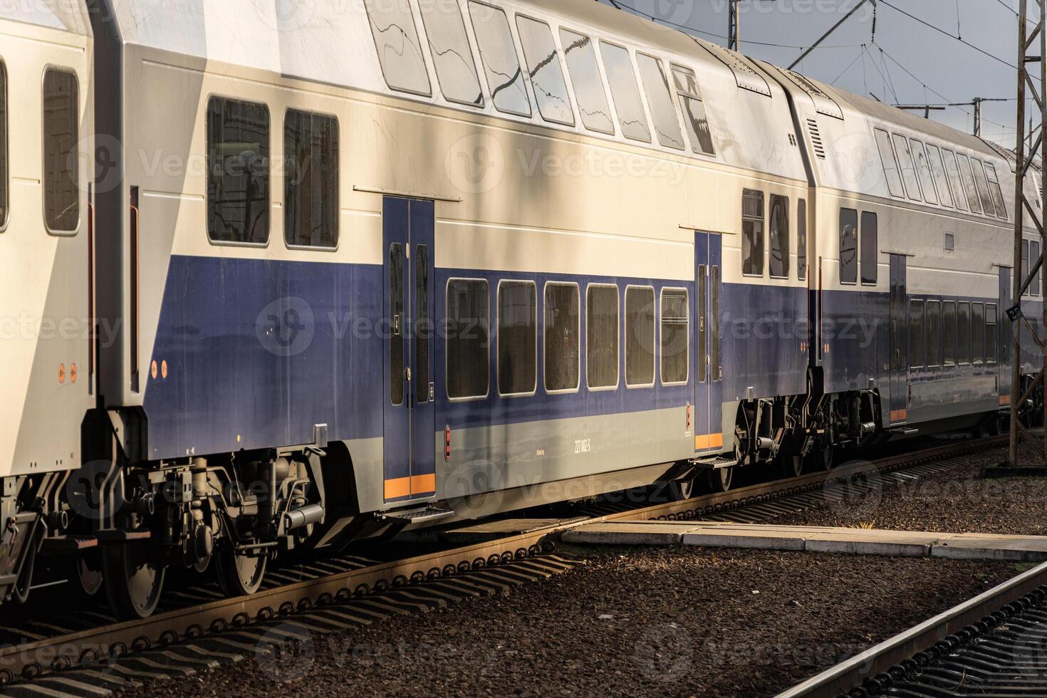 A sleek double-decker train is parked at the station, illuminated by warm late afternoon sunlight casting shadows on the tracks photo