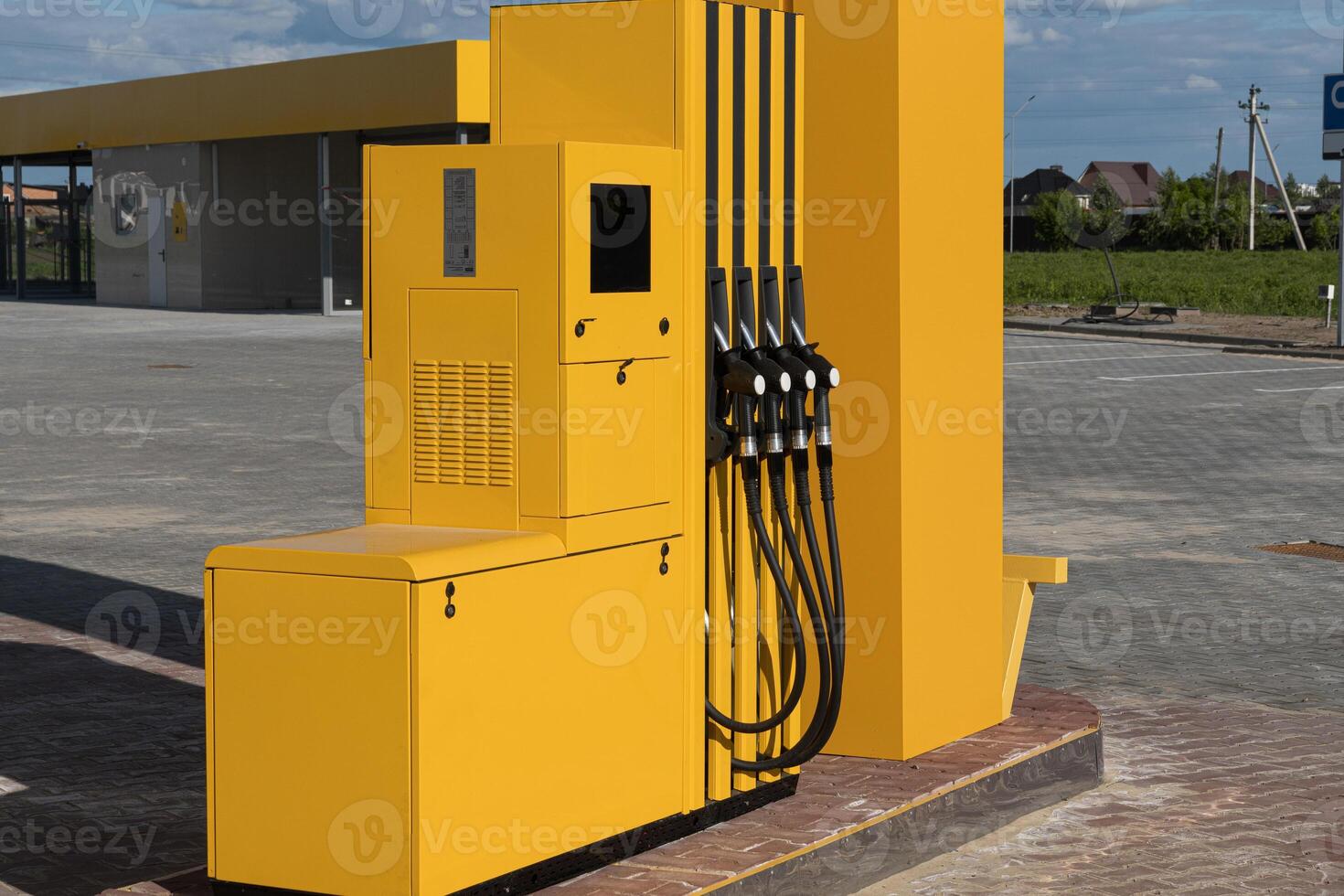 Fuel dispenser with multiple nozzles stands alone at a gas station, surrounded by open space and well-maintained surfaces under a clear sky photo