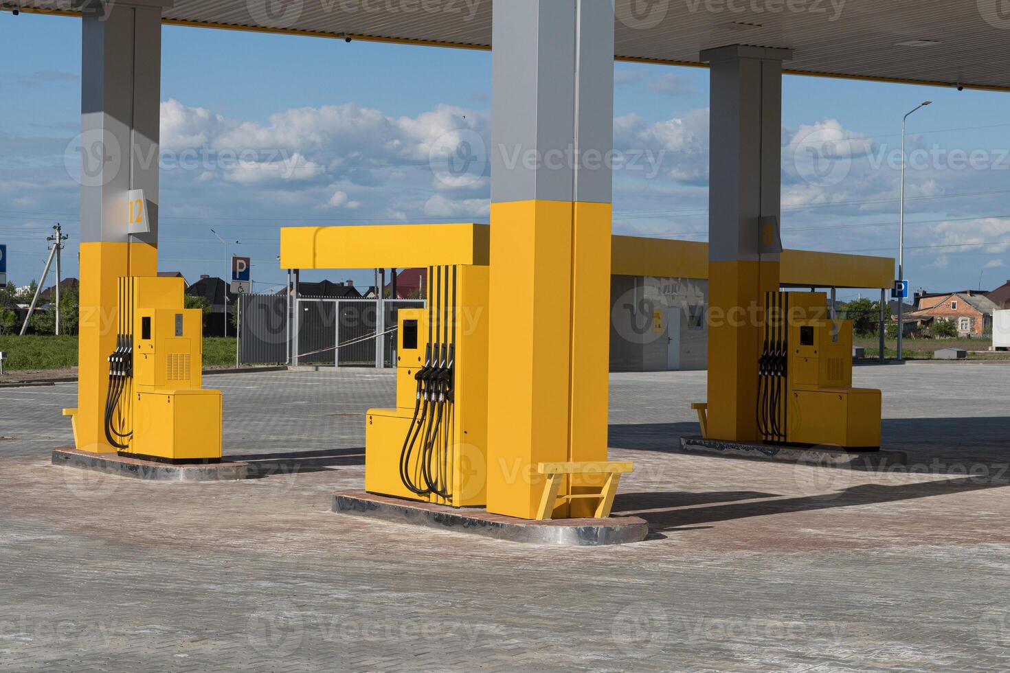 Empty gas station features several yellow fuel dispensers under a bright sky, illustrating a typical fueling location photo