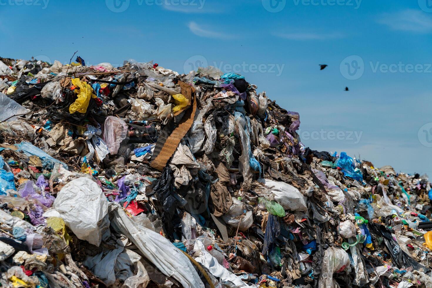 A vast, towering pile of mixed debris and plastic waste fills an urban landfill under a clear blue sky, illustrating a pressing environmental crisis photo