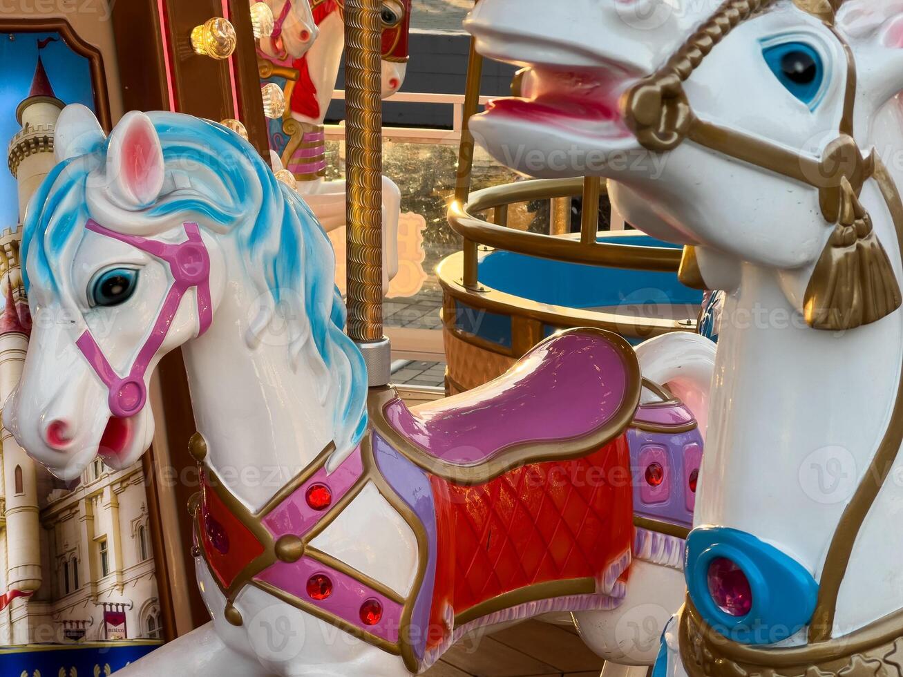 Two vibrant carousel horses with detailed designs stand ready for children at an amusement park, illuminated by the evening glow photo