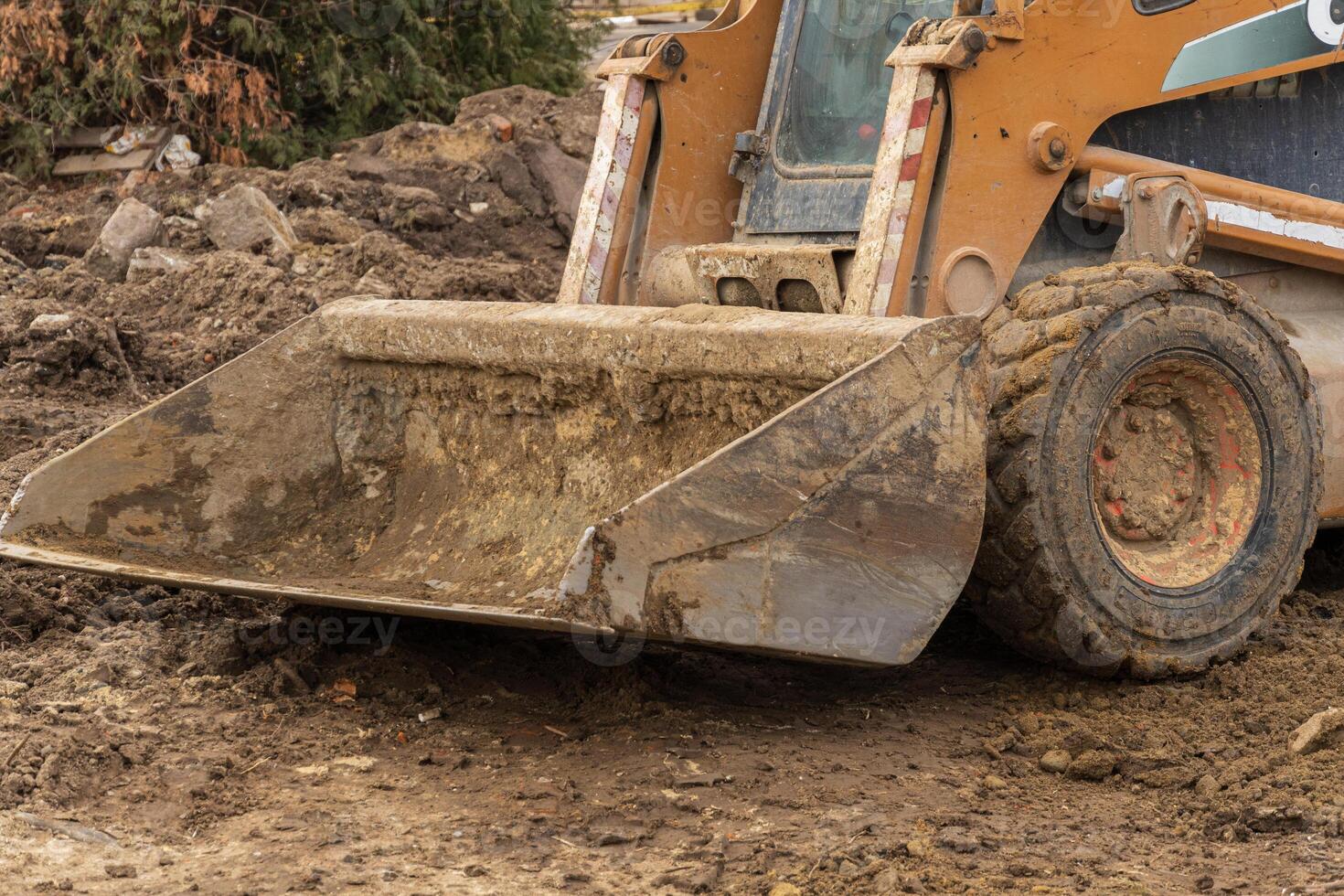 A skid steer loader is actively moving dirt and debris at a construction site on a cloudy day, showcasing the work in progress photo