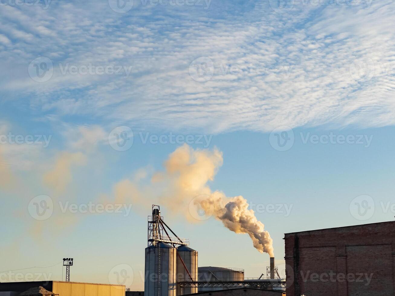 Industrial structures release smoke into the sky while the sun sets, creating a striking view of urban manufacturing activity photo