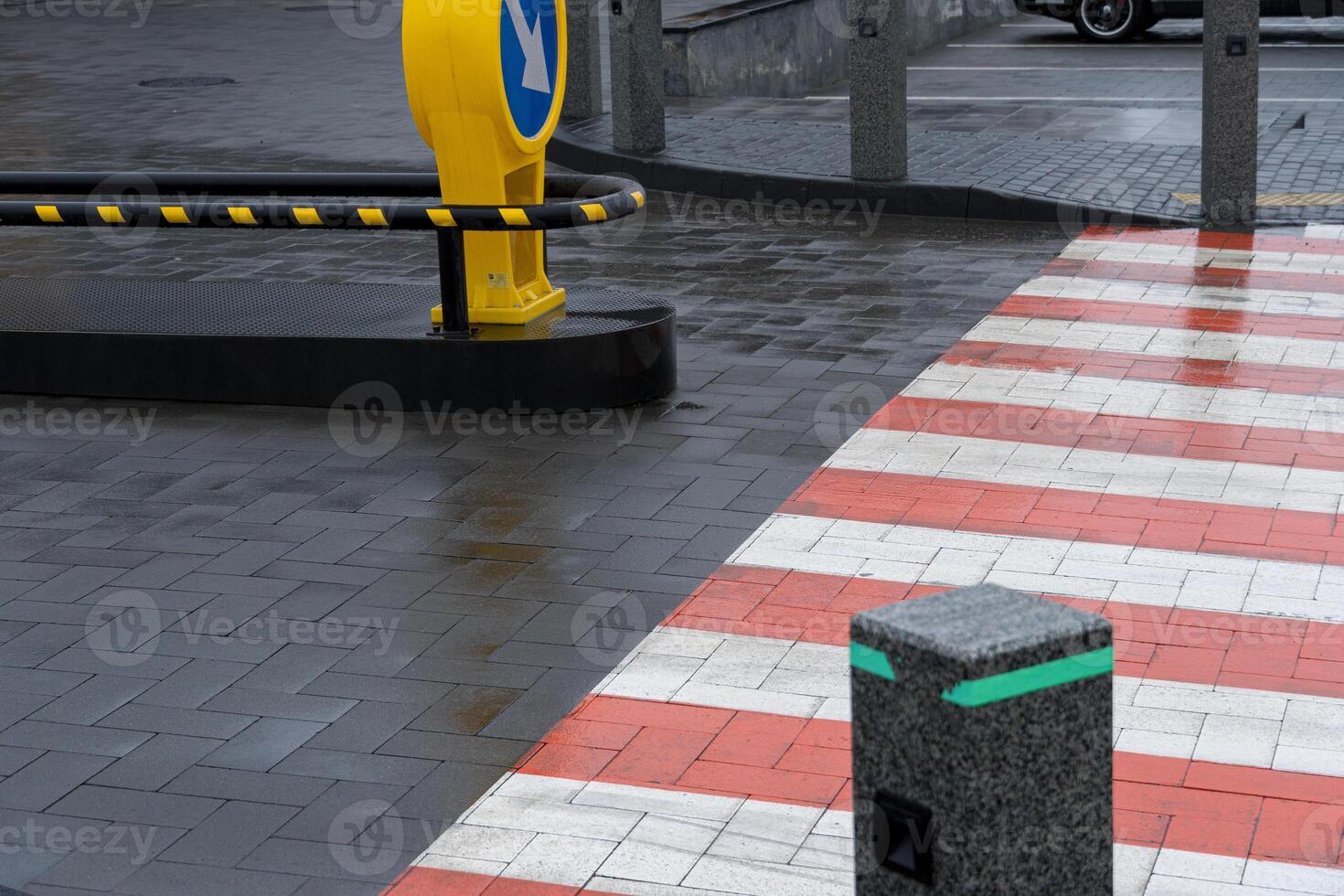 Wet pavement reflects surroundings while a yellow directional sign indicates traffic flow near a pedestrian crosswalk photo