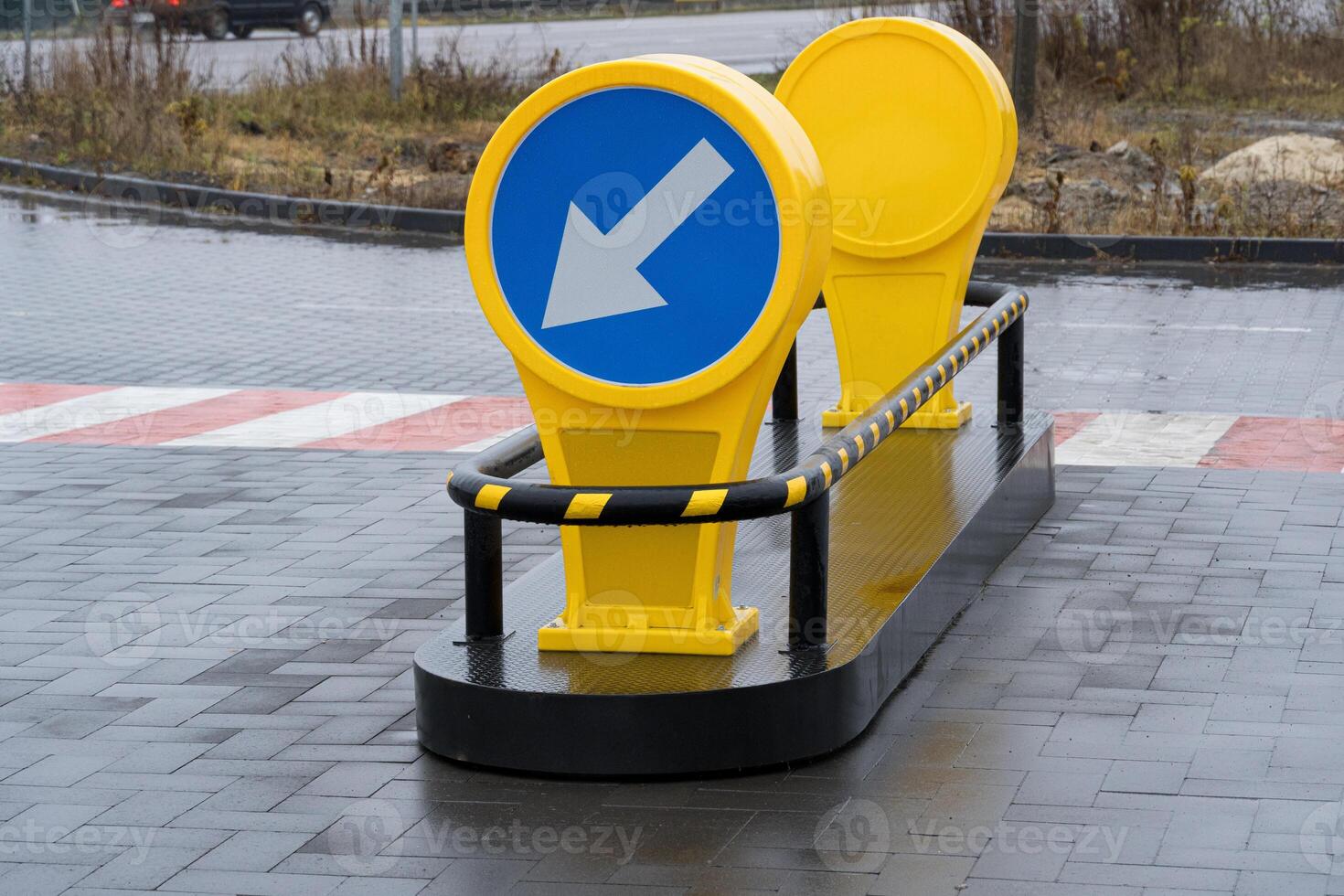 Bright yellow traffic barriers indicate the direction for vehicles on a rainy day along a paved roadside with wet surfaces photo