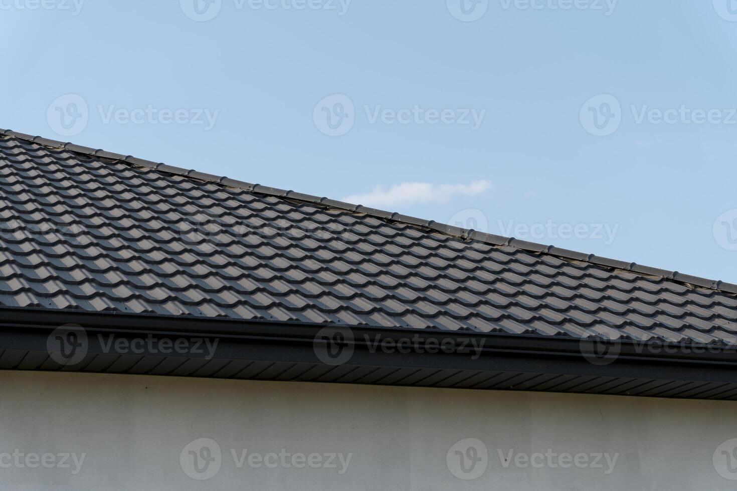 Freshly installed tiles cover the sloping roof of a modern home, providing durability and aesthetic appeal against a bright sky photo