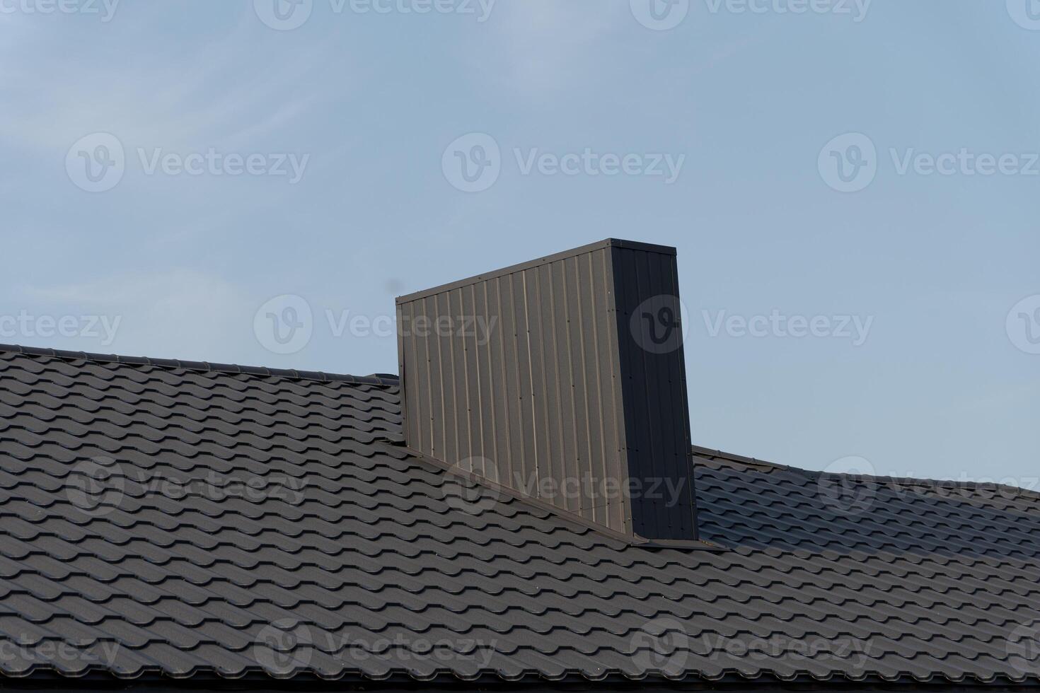 A unique vertical structure is situated atop a sloped roof, contrasting against the blue sky, showcasing modern design elements photo