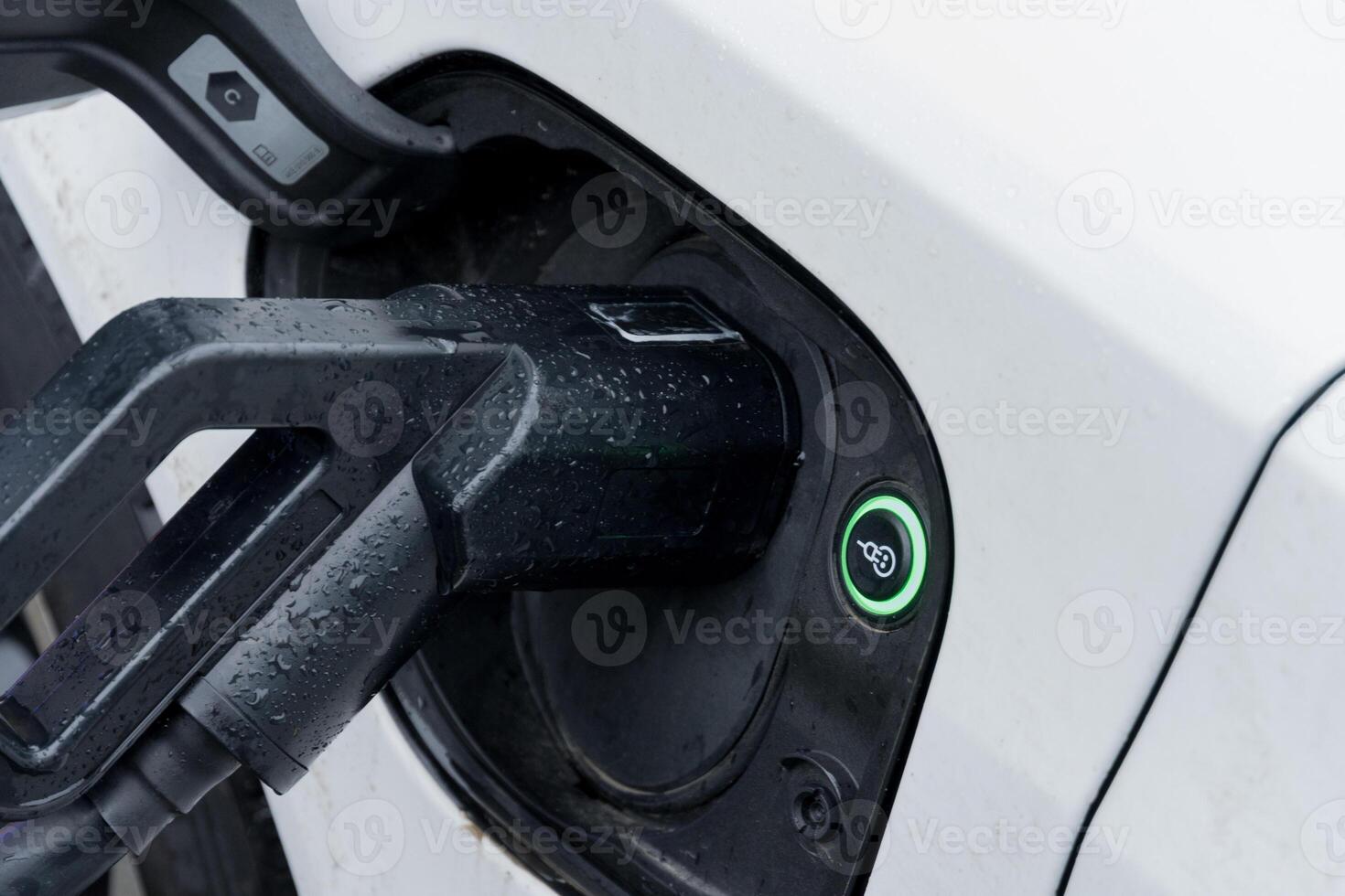 A charging connector is plugged into an electric vehicle at a station on a wet day, showcasing the growing trend of eco-friendly transport photo