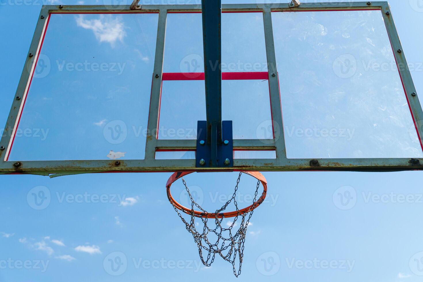 A weathered basketball hoop and net are positioned against a bright blue sky, showcasing a peaceful afternoon atmosphere photo