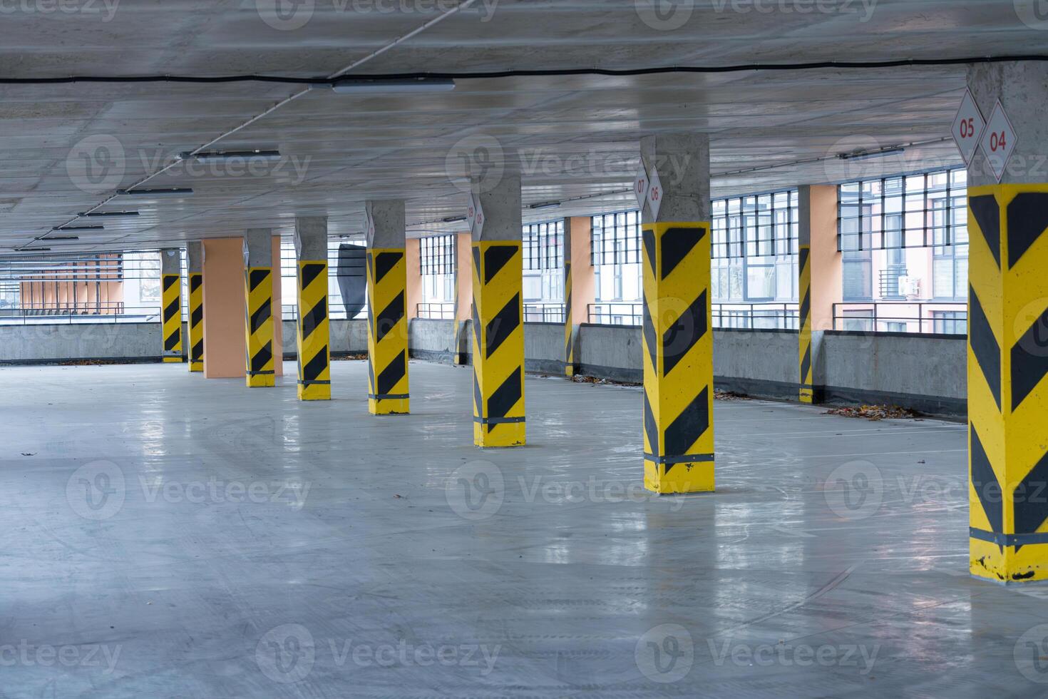 Spacious parking garage features yellow and black striped columns, large windows allowing natural light, and a clean concrete floor photo