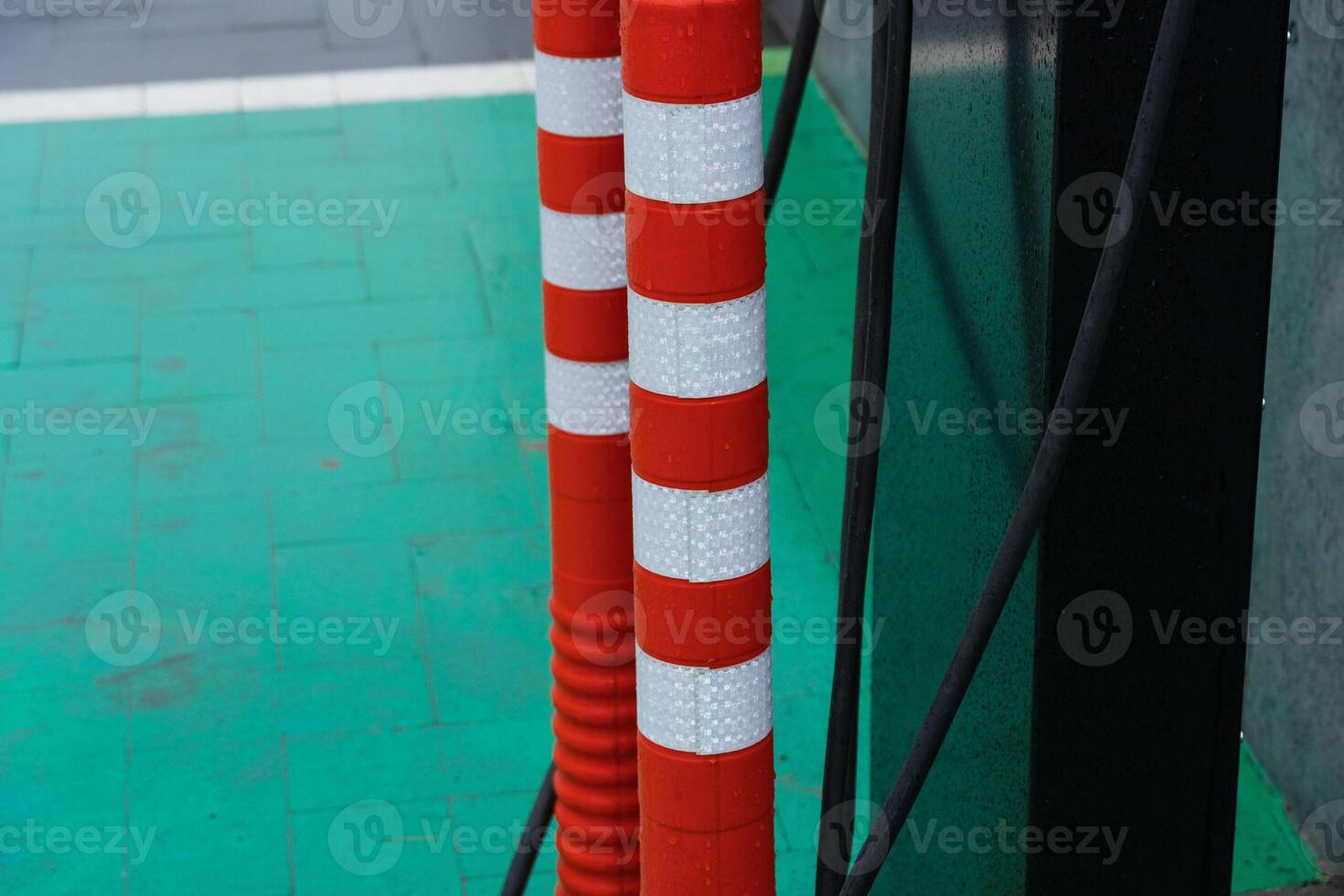 Two red and white striped poles stand next to a green pavement, with power cables nearby, capturing an urban, busy atmosphere photo