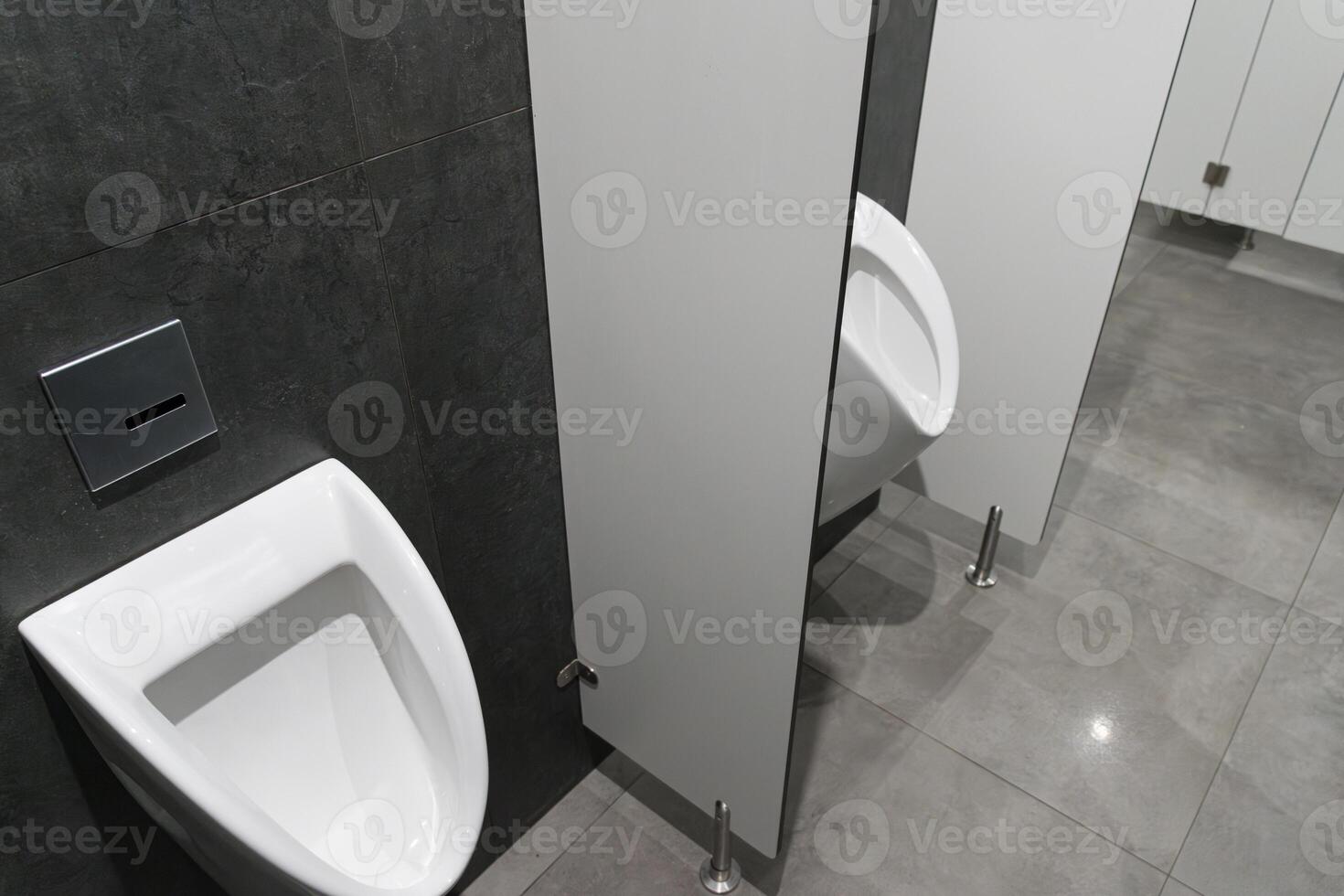 A contemporary restroom showcases a white urinal beside closed privacy stalls, all set against dark gray walls and tiled flooring photo