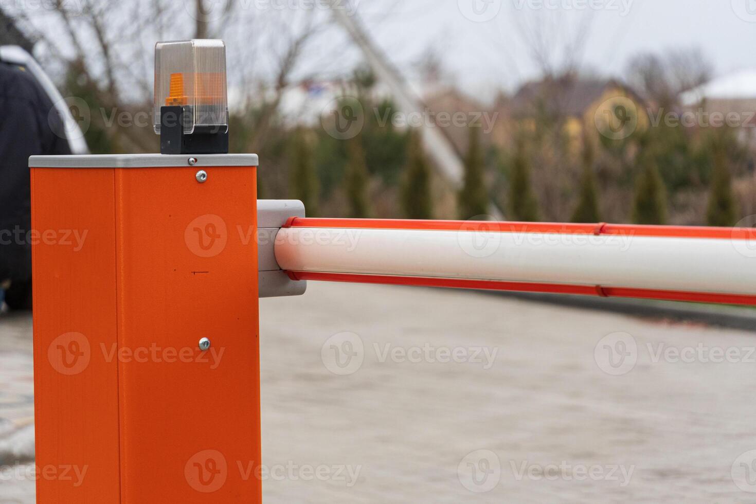 A bright orange barrier gate stands at the entrance of a parking lot, with a flashing light indicating restricted access to vehicles photo