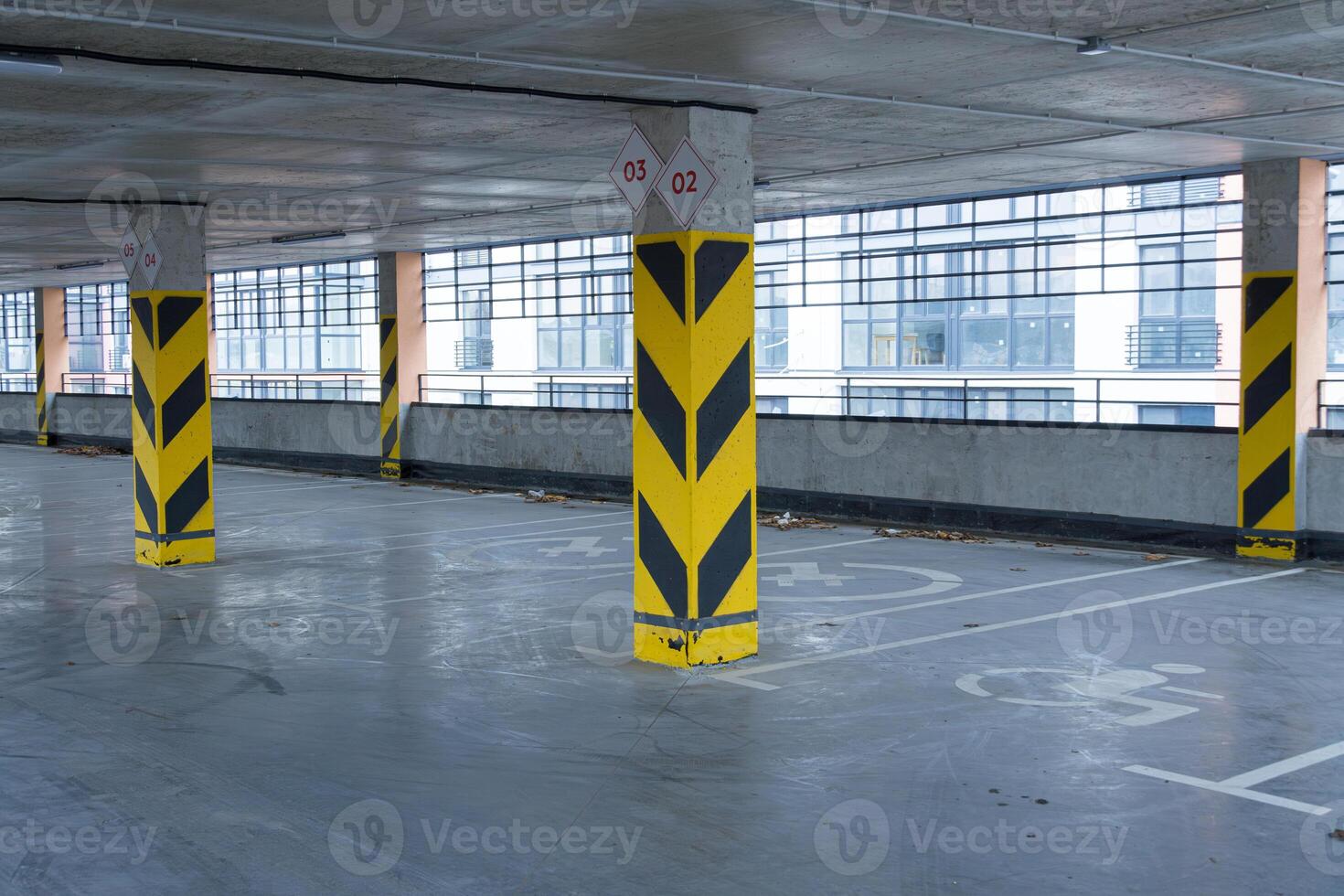 Empty parking garage showcases yellow striped columns with sleek, large windows visible in the background, highlighting an urban environment photo