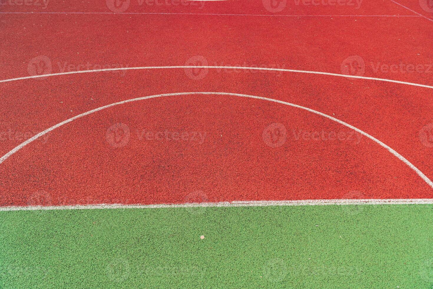 A basketball court surface features striking red and green areas, with clear markings visible under bright afternoon sunlight photo