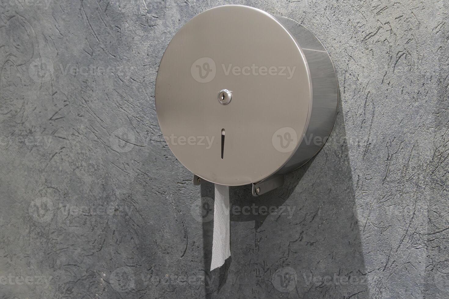 A sleek stainless steel toilet paper dispenser is attached to a textured wall, with a portion of the roll extending out for use photo