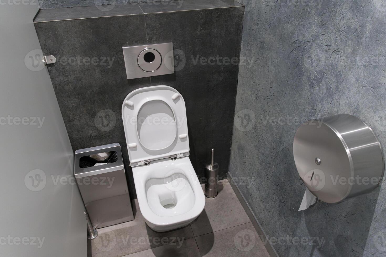 A well-maintained restroom showcases a white toilet, a metal trash bin, and a sleek paper towel dispenser in a contemporary space photo