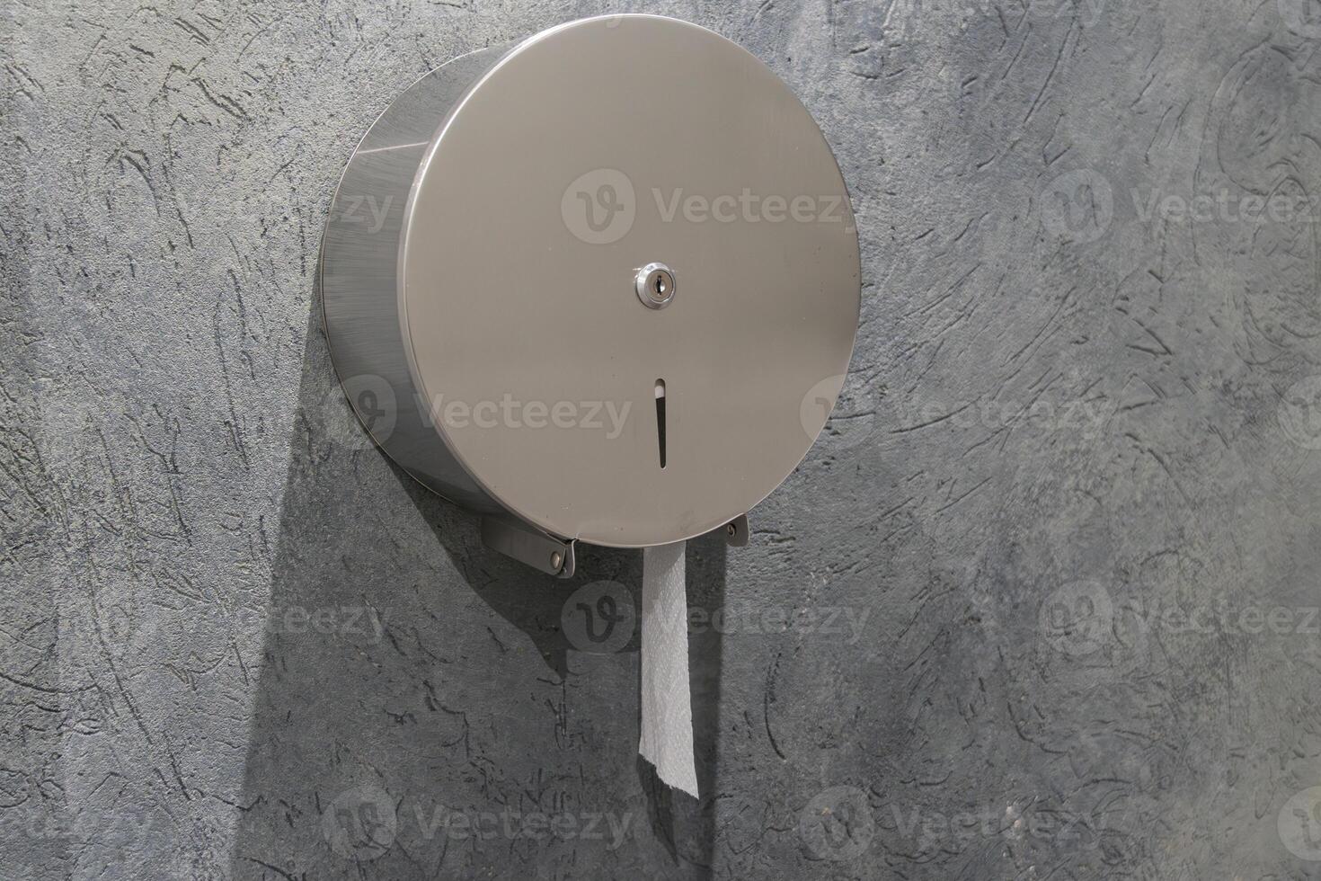 Metal paper towel dispenser affixed to a textured gray wall, showcasing a clean and functional design often found in restrooms photo