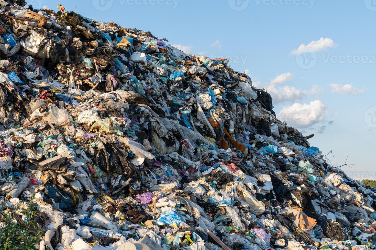 An expanse of everyday waste towers high, revealing the environmental crisis while a bright sky casts shadows over the debris photo