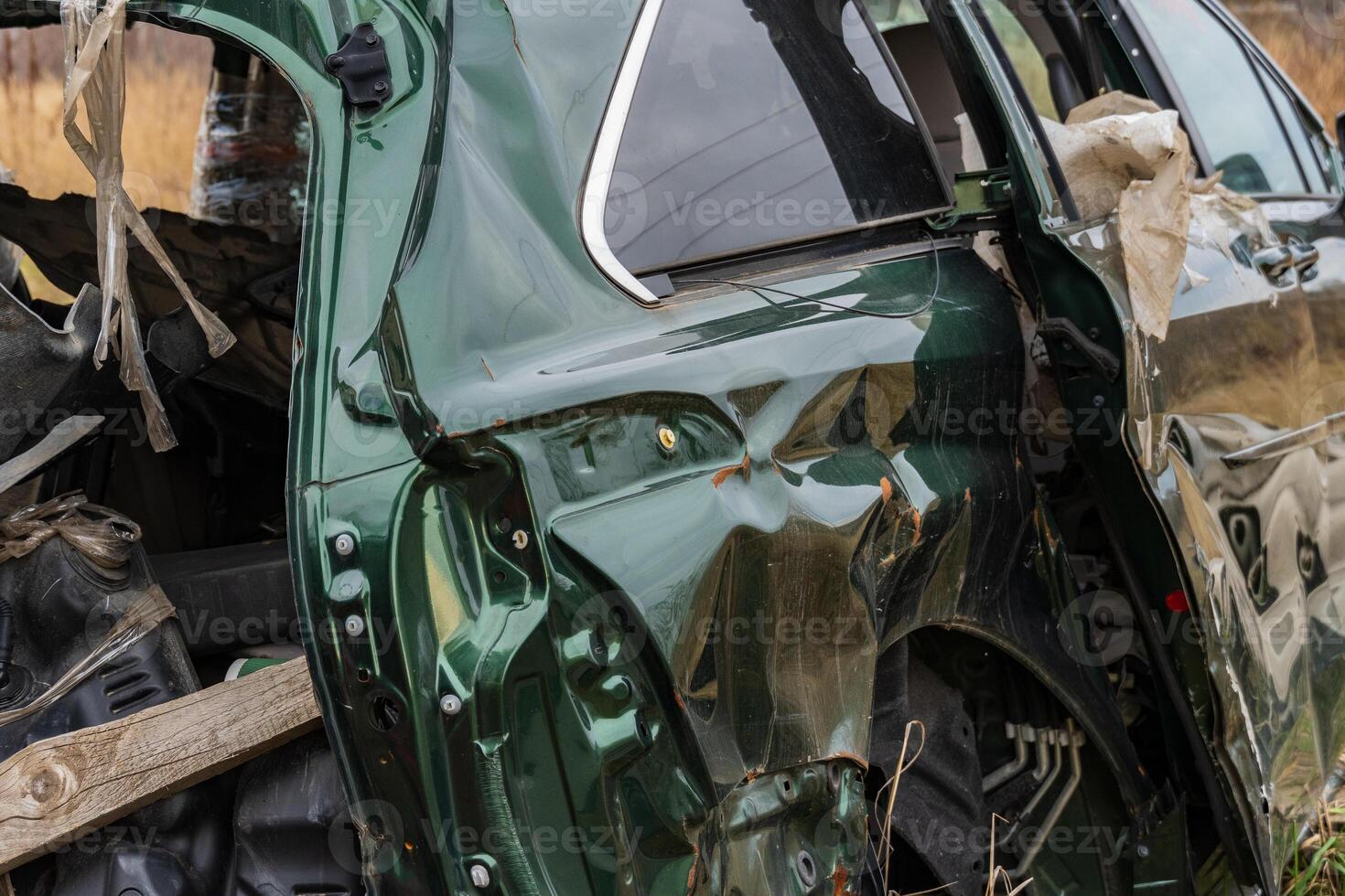 An abandoned automobile rests in a field, showcasing the damage of a past accident, juxtaposed against the natural landscape surrounding it photo